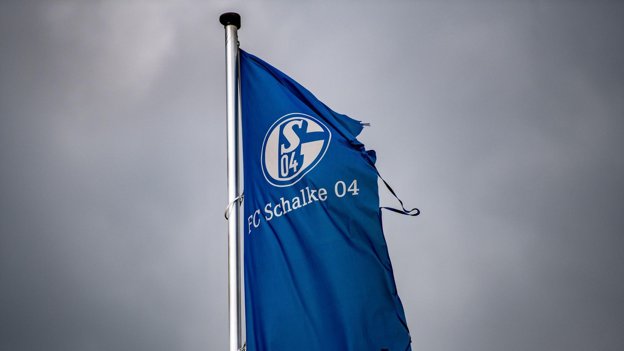 Eine zerrissene Schalke-Fahne weht über der Veltins-Arena in Gelsenkirchen mit einem dunklen Himmel im HIntergrund.