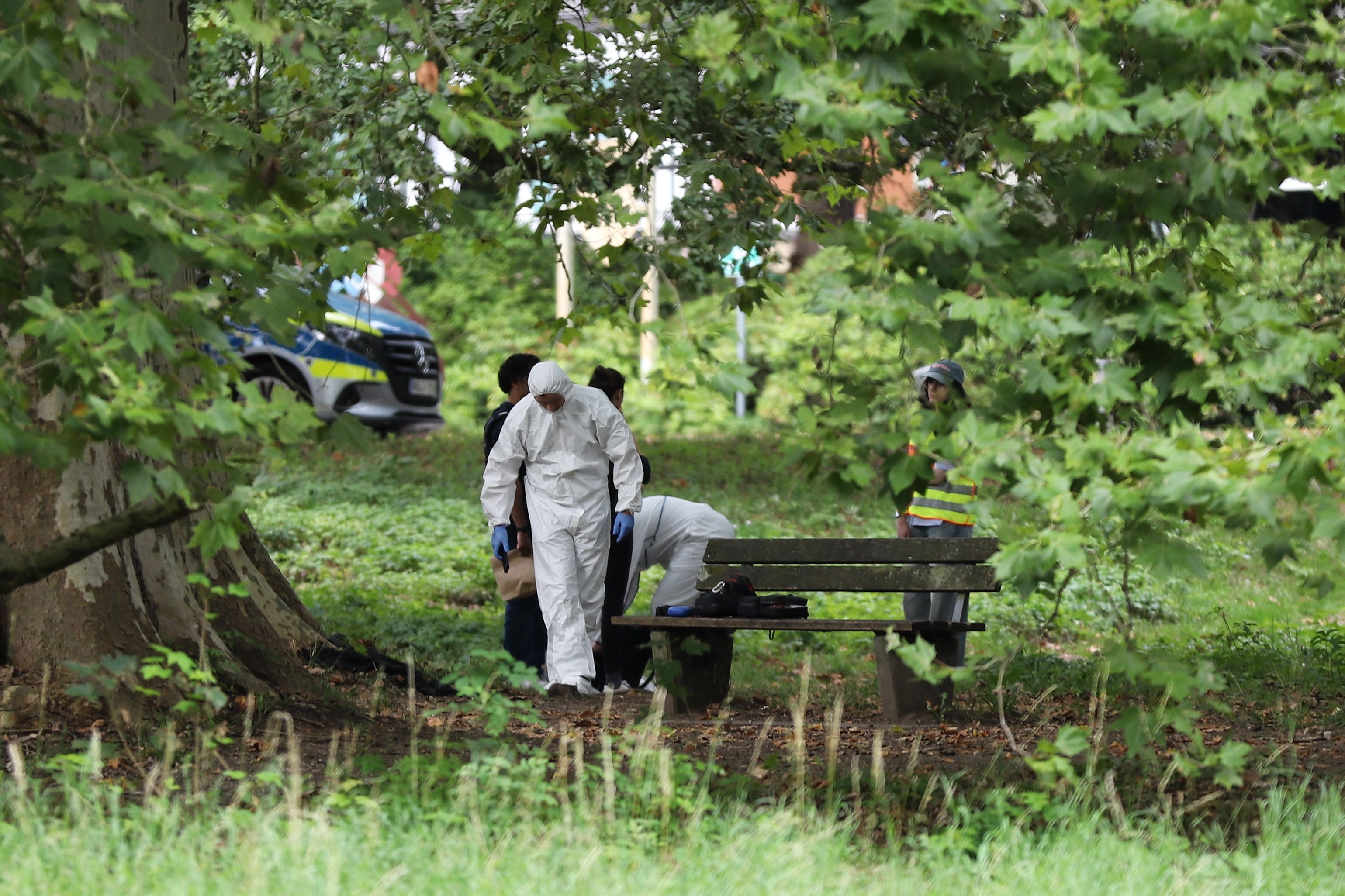 Einsatzkräfte der Polizei in Schutzkleidung arbeiten an einem Tatort in einem Park.