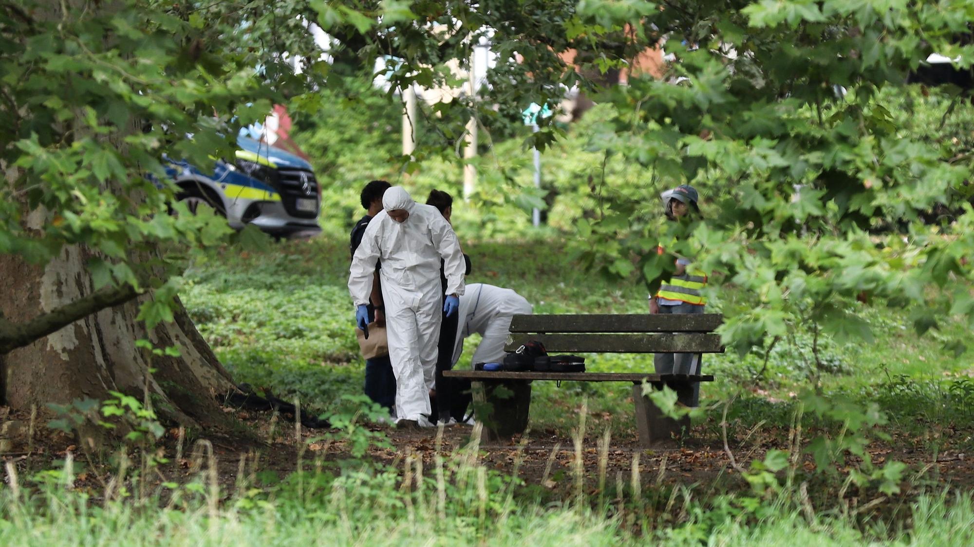 Einsatzkräfte der Polizei in Schutzkleidung arbeiten an einem Tatort in einem Park.