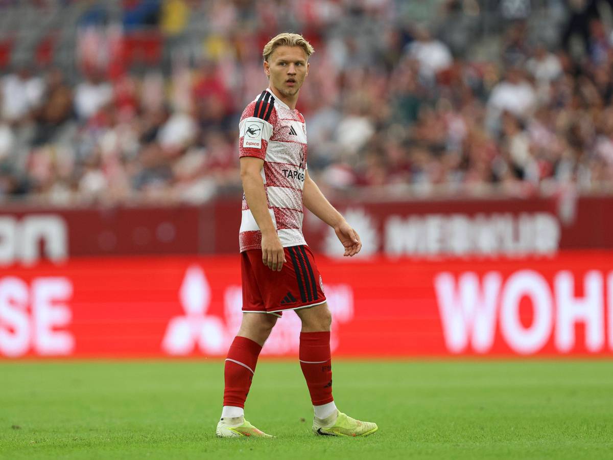 Andreas Müller steht auf dem Rasen und blickt zur Seite. Er trägt ein rot-weißes Trikot von Fortuna Düsseldorf.