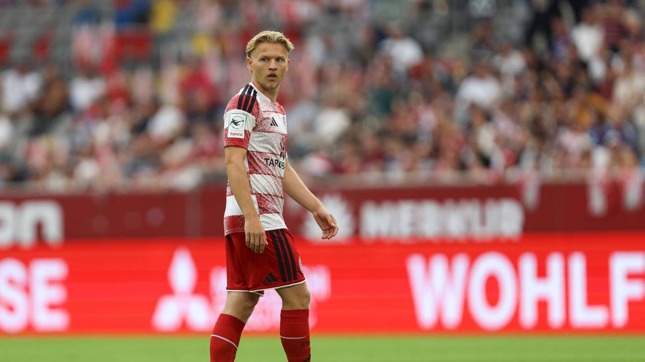 Andreas Müller steht auf dem Rasen und blickt zur Seite. Er trägt ein rot-weißes Trikot von Fortuna Düsseldorf.