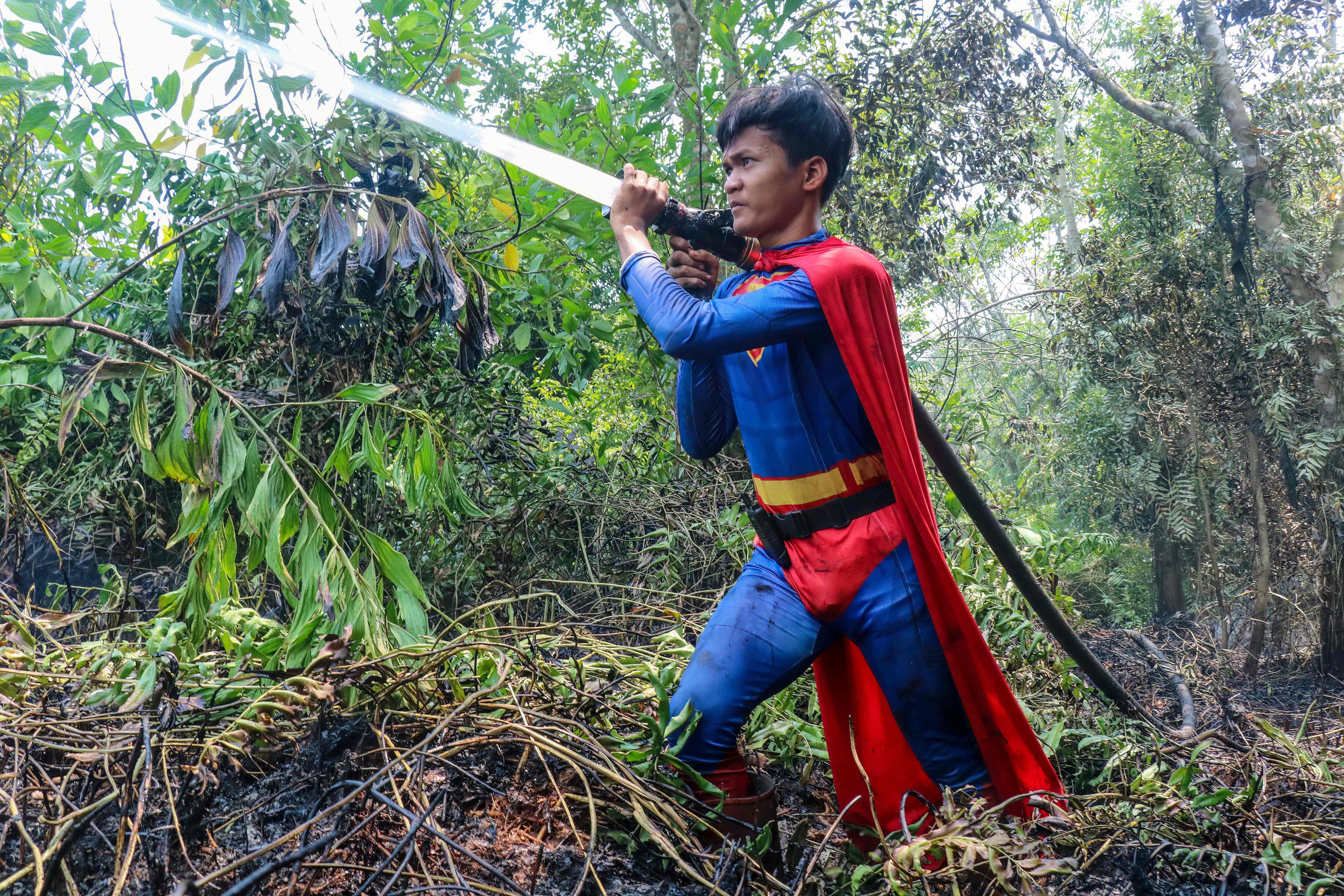 In this photo taken on August 17, 2026 Indonesian student Rudiansyah dressed in a Superman costume helps to extinguish a forest and land fire at Petuk Katimpun in Palangkaraya, Central Kalimantan. (Photo by REINA / AFP)
