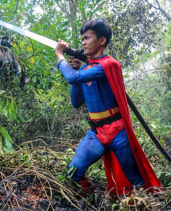 In this photo taken on August 17, 2026 Indonesian student Rudiansyah dressed in a Superman costume helps to extinguish a forest and land fire at Petuk Katimpun in Palangkaraya, Central Kalimantan. (Photo by REINA / AFP)