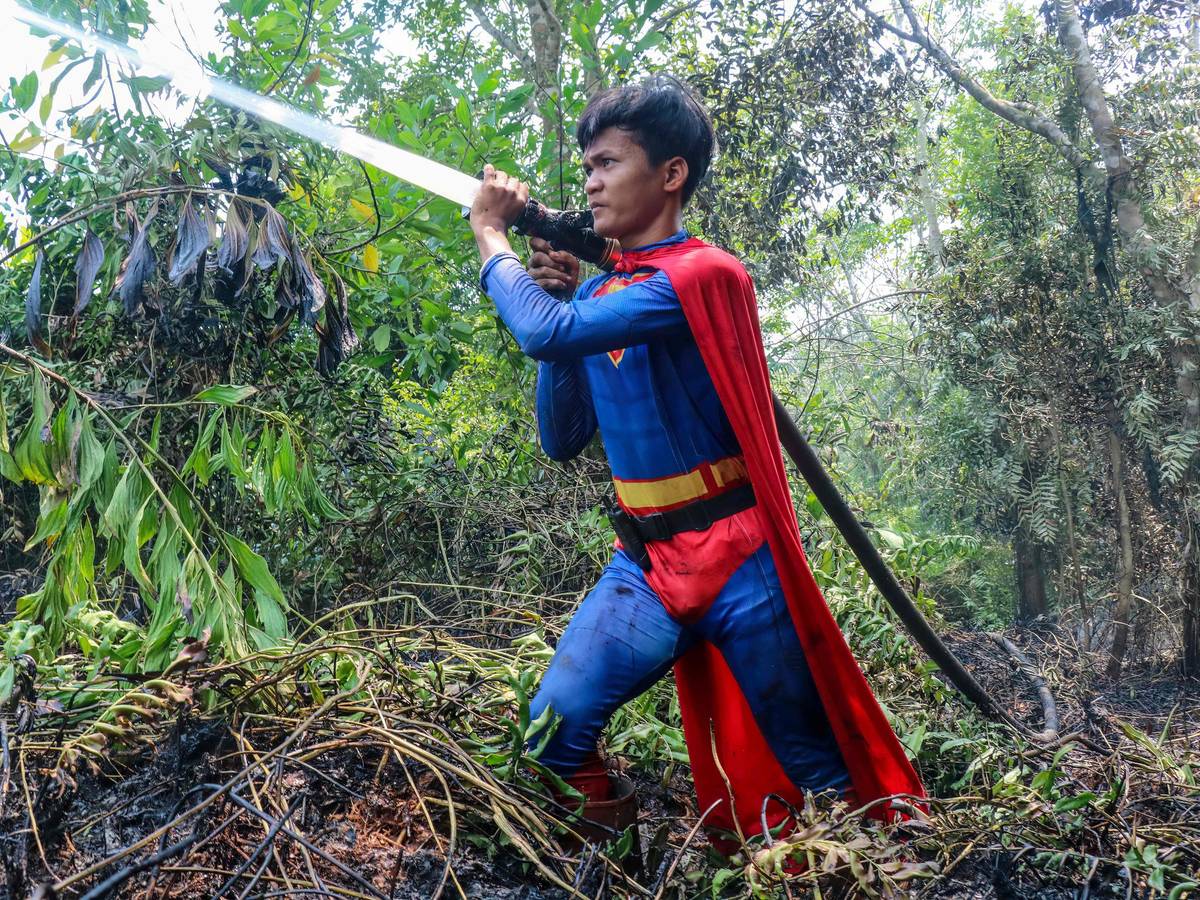In this photo taken on August 17, 2026 Indonesian student Rudiansyah dressed in a Superman costume helps to extinguish a forest and land fire at Petuk Katimpun in Palangkaraya, Central Kalimantan. (Photo by REINA / AFP)