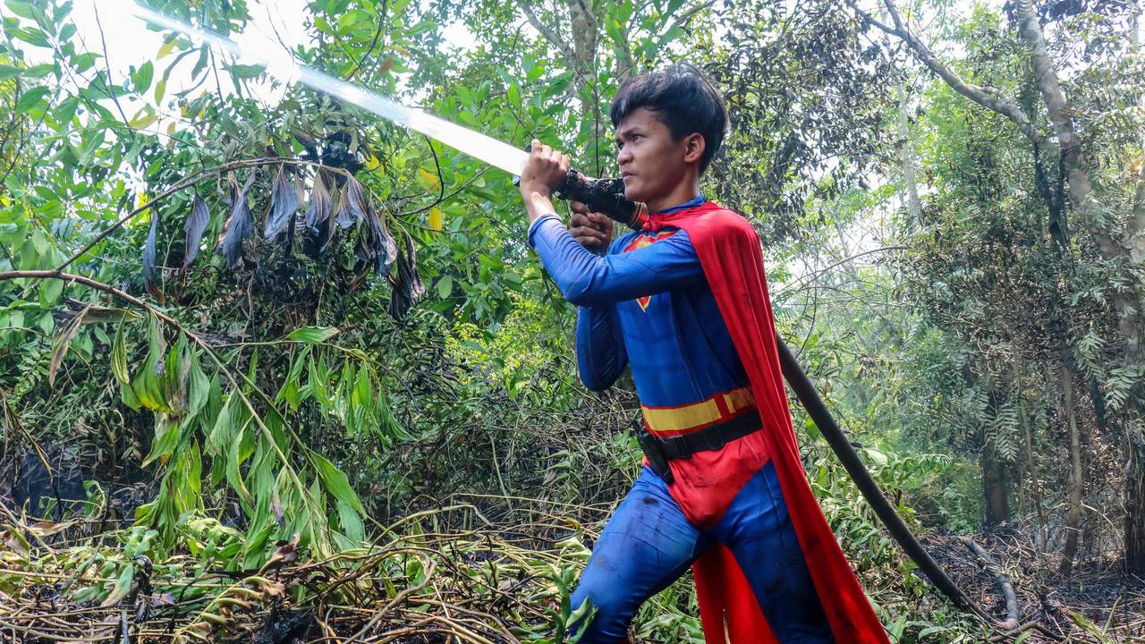 In this photo taken on August 17, 2026 Indonesian student Rudiansyah dressed in a Superman costume helps to extinguish a forest and land fire at Petuk Katimpun in Palangkaraya, Central Kalimantan. (Photo by REINA / AFP)
