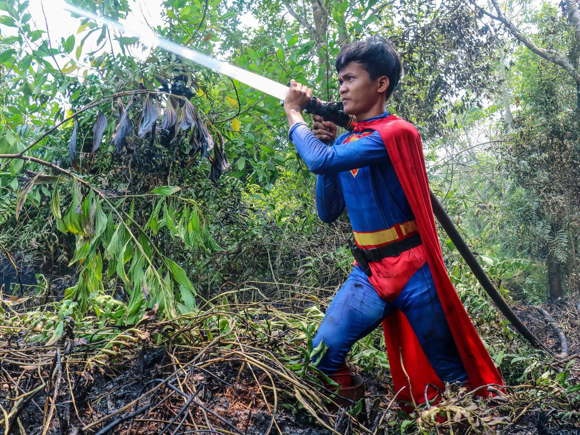 In this photo taken on August 17, 2026 Indonesian student Rudiansyah dressed in a Superman costume helps to extinguish a forest and land fire at Petuk Katimpun in Palangkaraya, Central Kalimantan. (Photo by REINA / AFP)