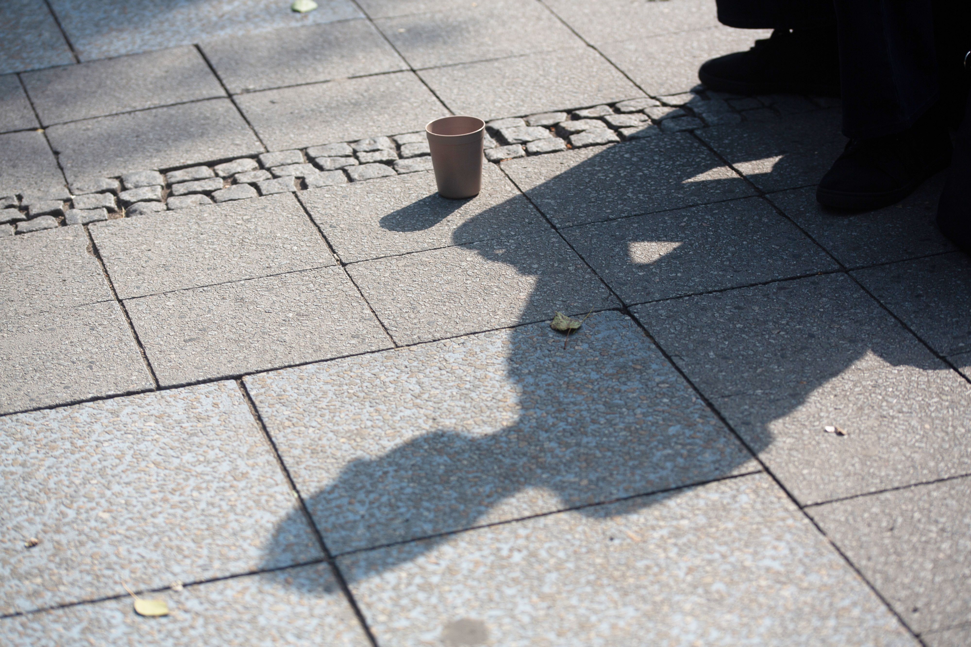 Der Schatten einer Person mit einem Becher für Spenden fällt auf den Gehweg. Im Juli hatte es eine Debatte zu einem möglichen Bettelverbot in Köln gegeben. (Archivfoto)