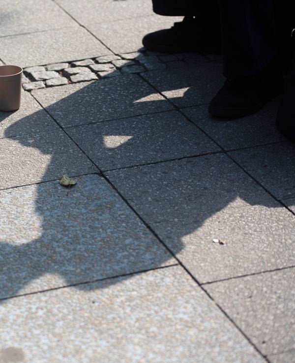 Der Schatten einer Person mit einem Becher für Spenden fällt auf den Gehweg. Im Juli hatte es eine Debatte zu einem möglichen Bettelverbot in Köln gegeben. (Archivfoto)
