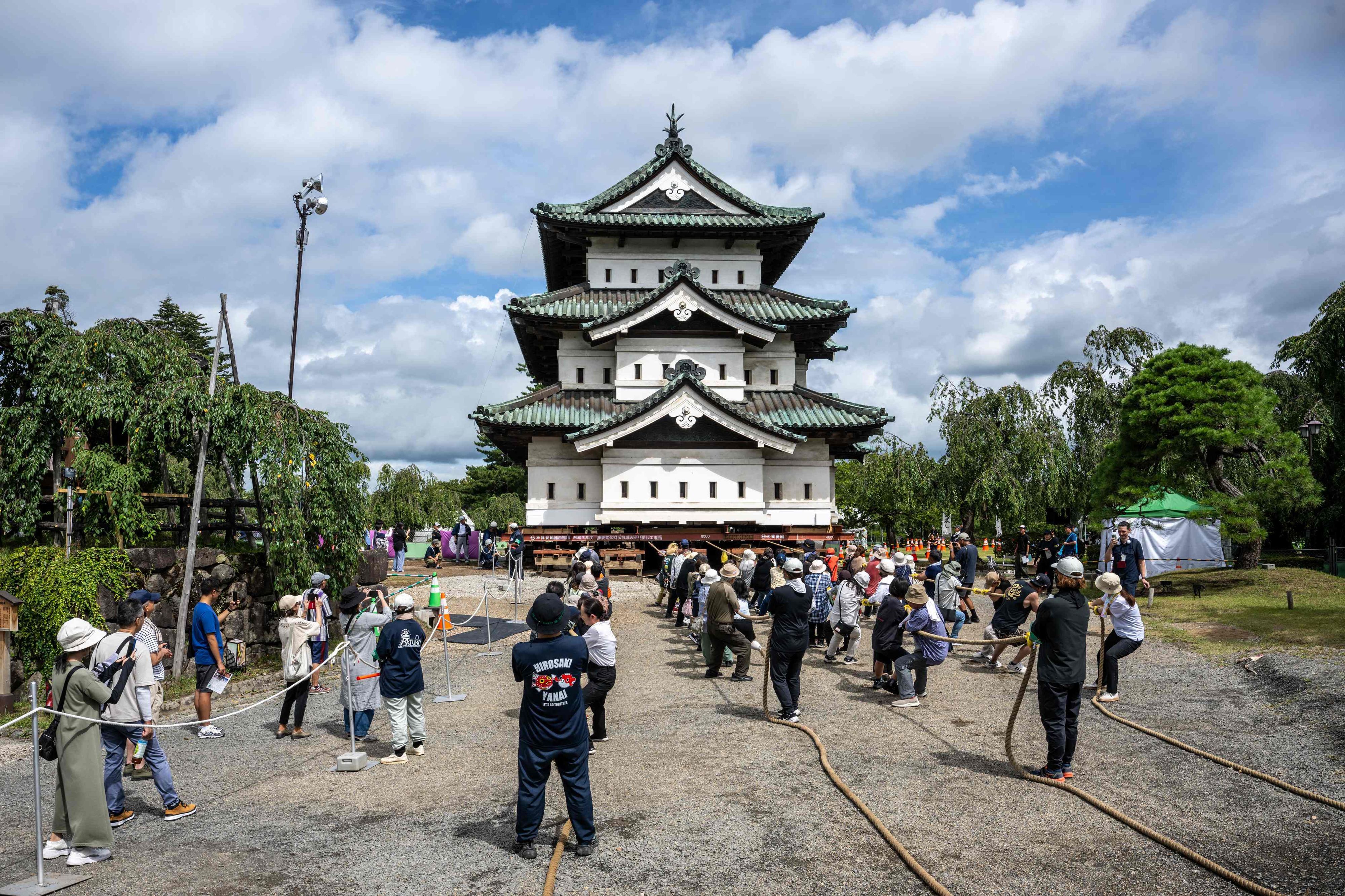 Besucher beobachten, wie Freiwillige den Burgturm Hirosaki nach den Restaurierungsarbeiten mit Seilen an ihren ursprünglichen Standort zurückziehen.