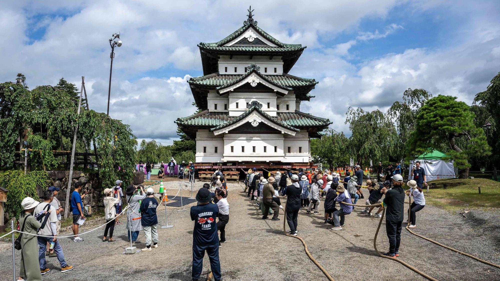 Besucher beobachten, wie Freiwillige den Burgturm Hirosaki nach den Restaurierungsarbeiten mit Seilen an ihren ursprünglichen Standort zurückziehen.