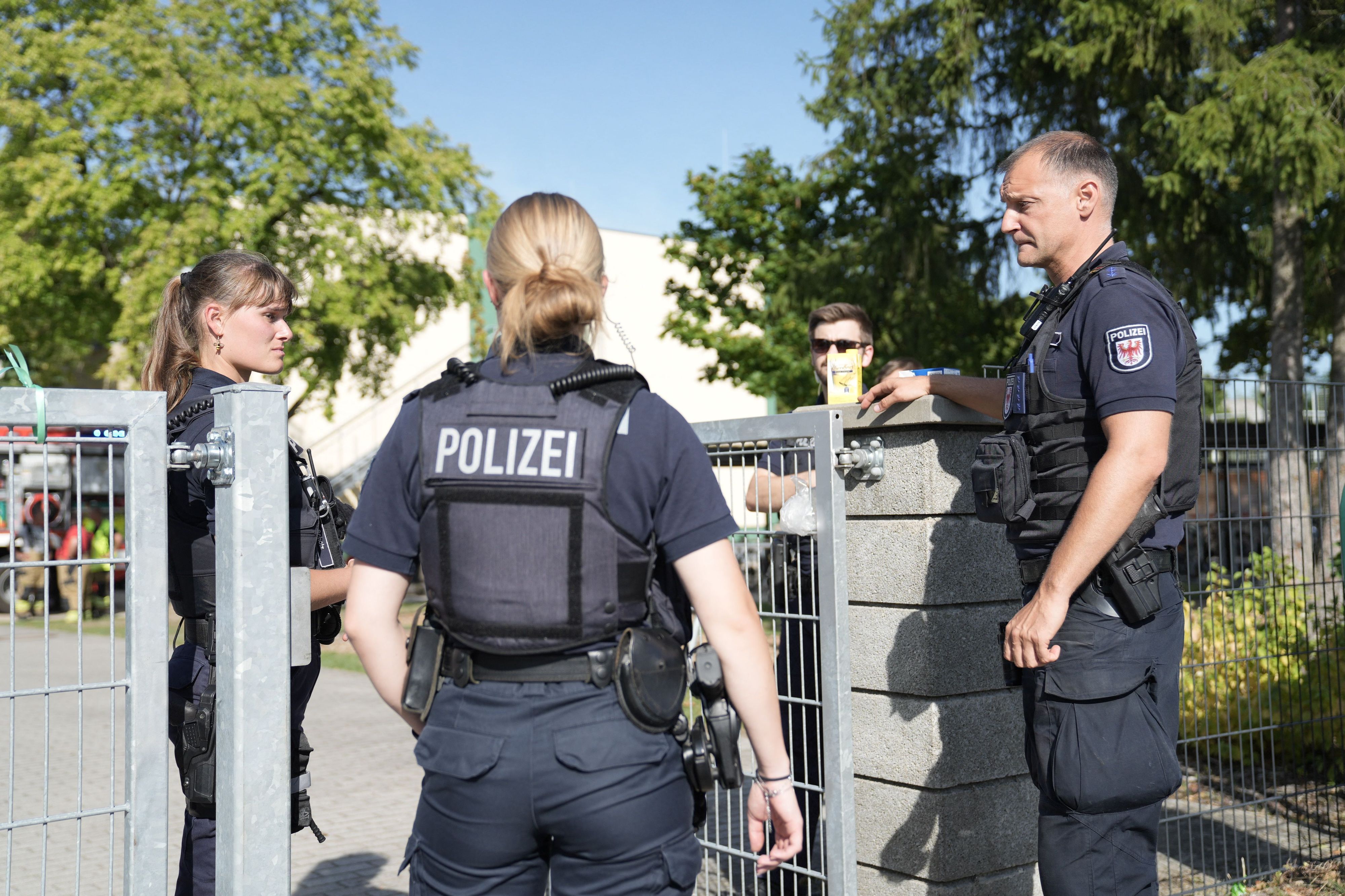 Zwei Polizisten und ein Polizist stehen vor einer Schule.