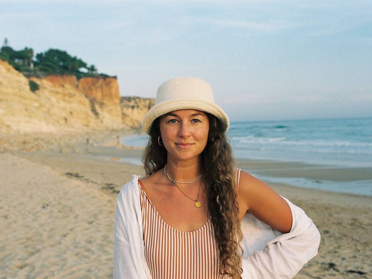 Eine Frau steht am Strand und lächelt in die Kamera.