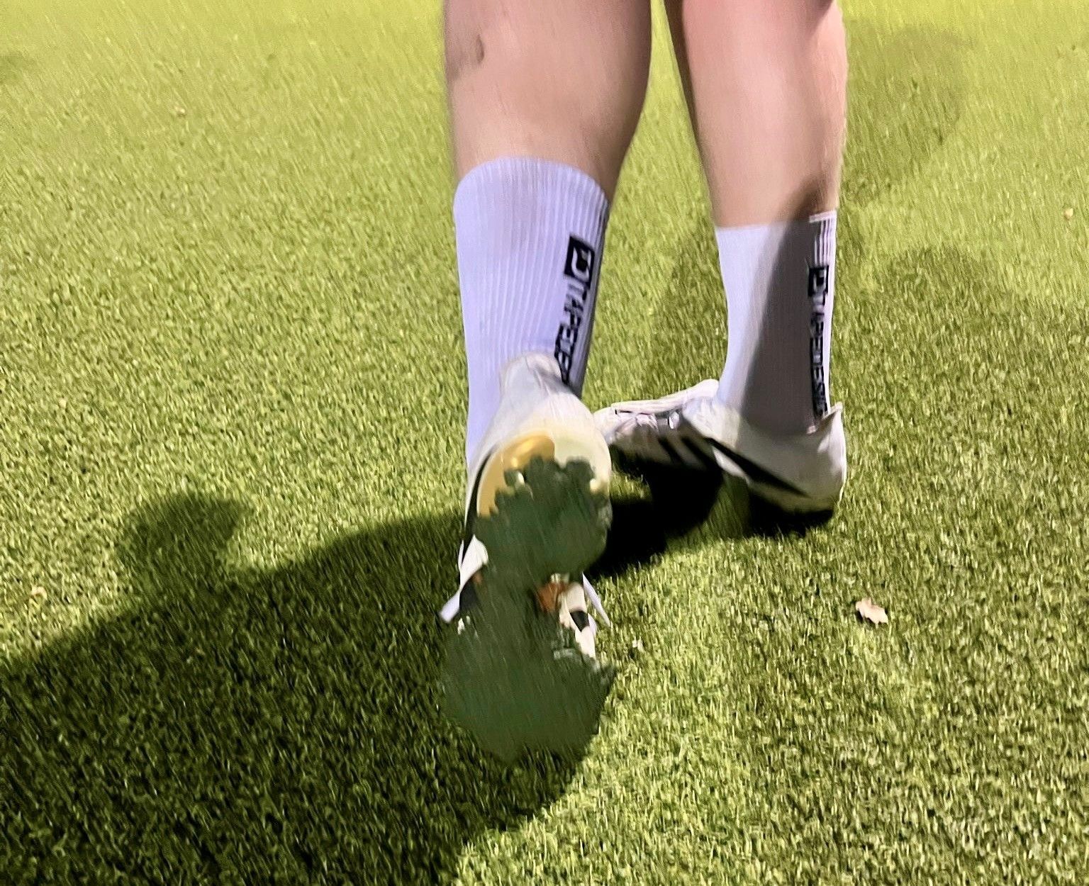 Kunstrasen-Granulat pappt unter den Schuhen eines Fußballspielers.