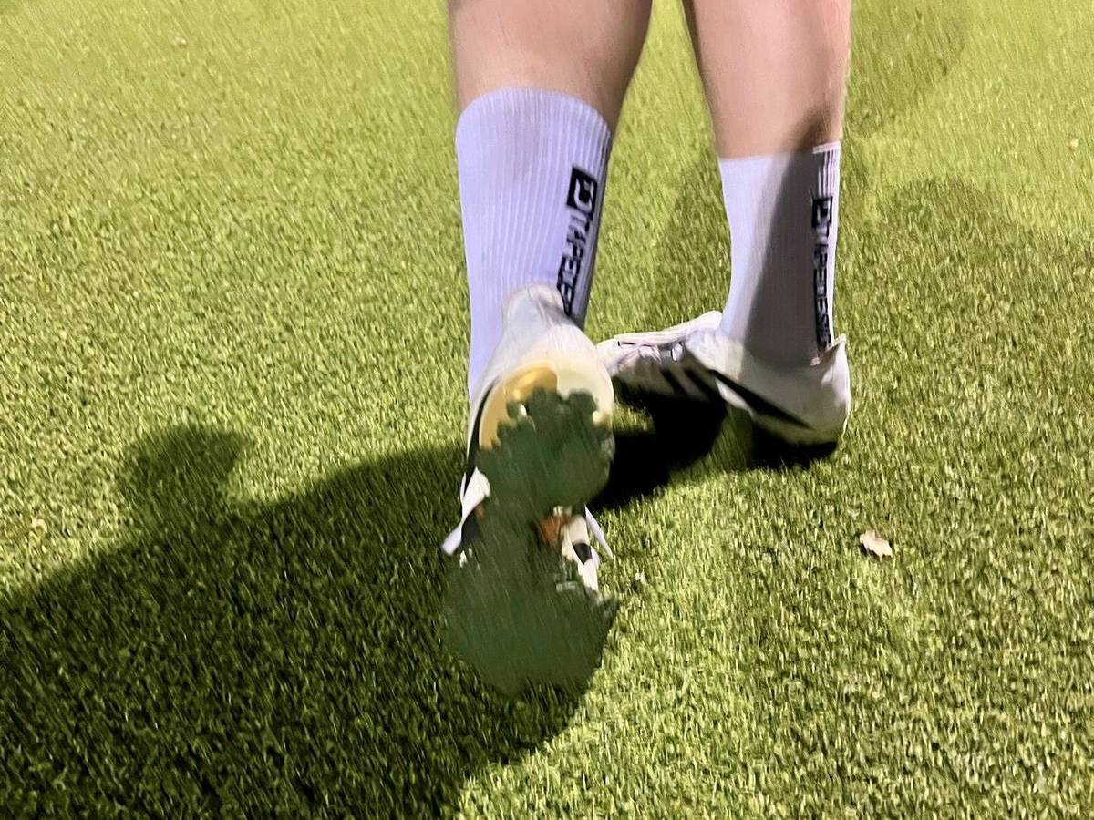 Ein Fußballspieler zeigt die Sohle seines Schuhes, unter dem eine Schicht des Kunstrasen-Granulats klebt.