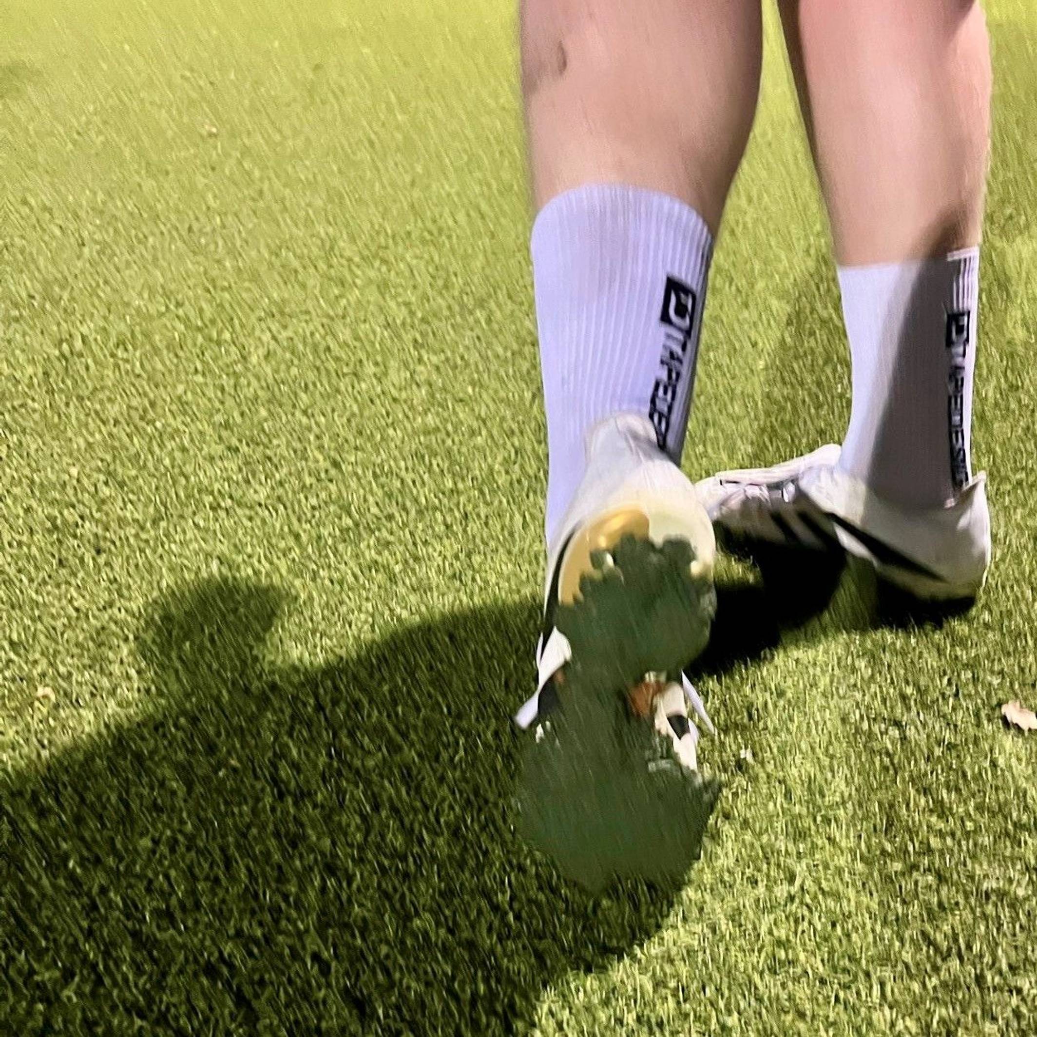 Ein Fußballspieler zeigt die Sohle seines Schuhes, unter dem eine Schicht des Kunstrasen-Granulats klebt.