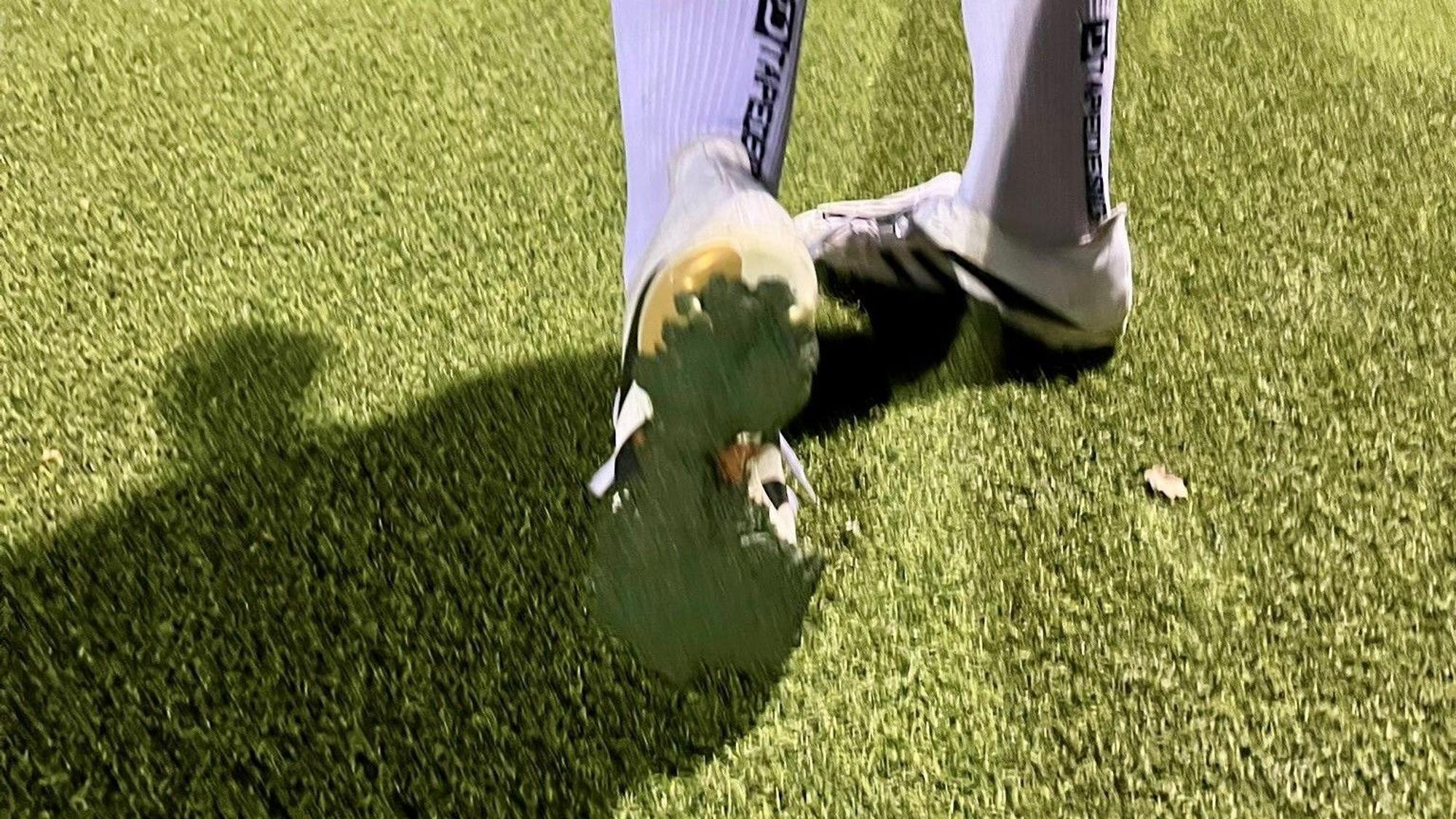 Ein Fußballspieler zeigt die Sohle seines Schuhes, unter dem eine Schicht des Kunstrasen-Granulats klebt.