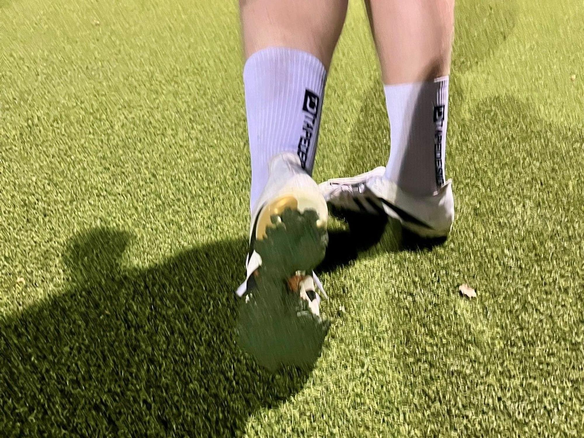 Kunstrasen-Granulat pappt unter den Schuhen eines Fußballspielers.