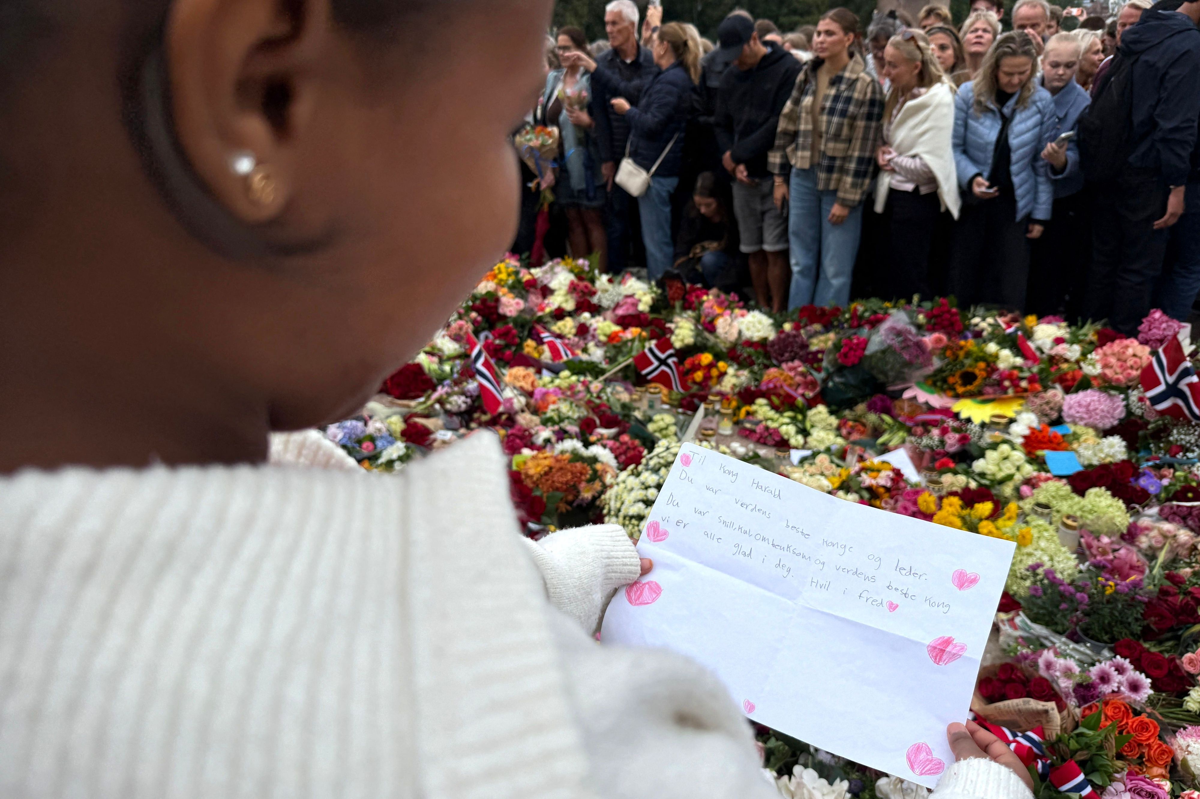 Die elfjährige Mina hält ihren selbstgeschriebenen Brief mit der Aufschrift „Du warst nett, cool, fürsorglich und der beste König der Welt“ zwischen den vor dem Königlichen Schloss Oslo abgelegten Blumen in den Händen.