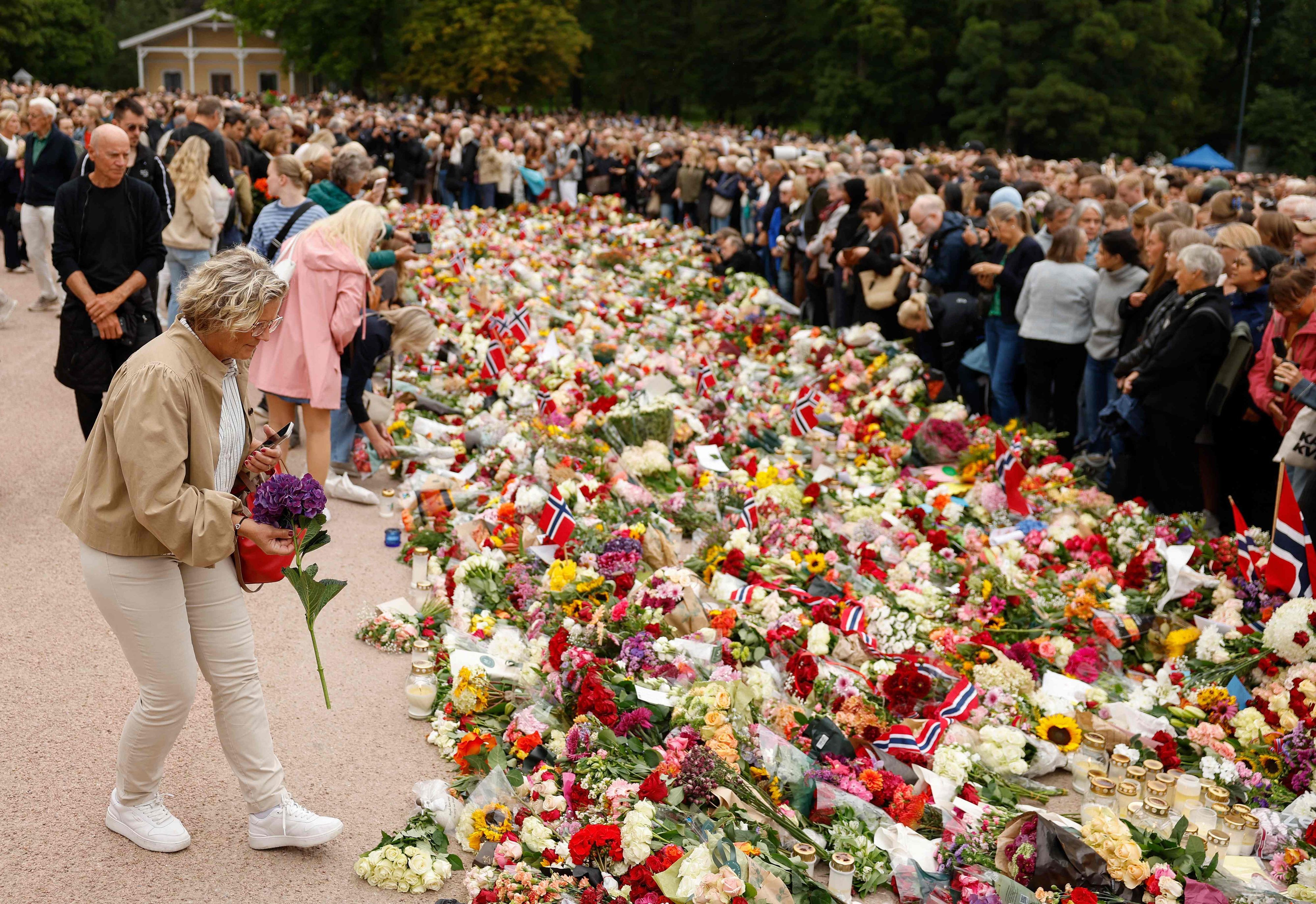 Der Platz vor dem Schloss verwandelt sich zunehmend in ein Blumenmeer, während Zehntausende Menschen kommen, um dem verstorbenen König die letzte Ehre zu erweisen.