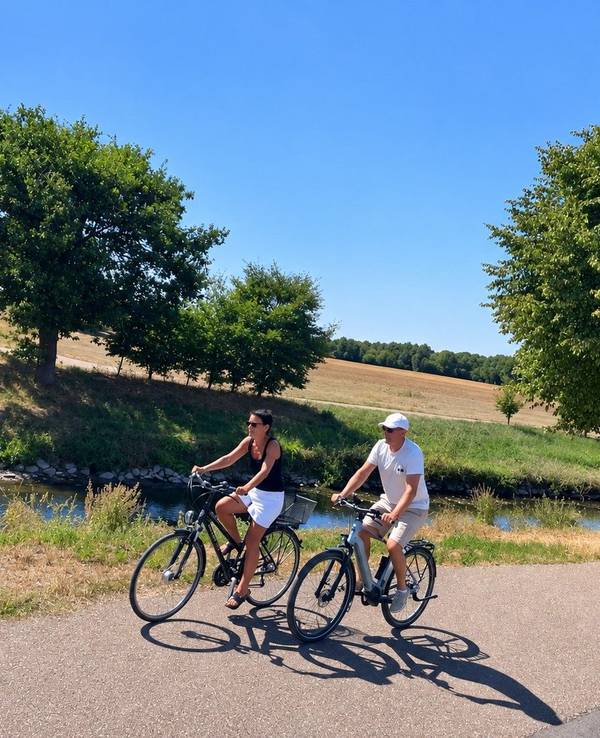 Zwei Radfahrer fahren durch eine sommerliche Flusslandschaft