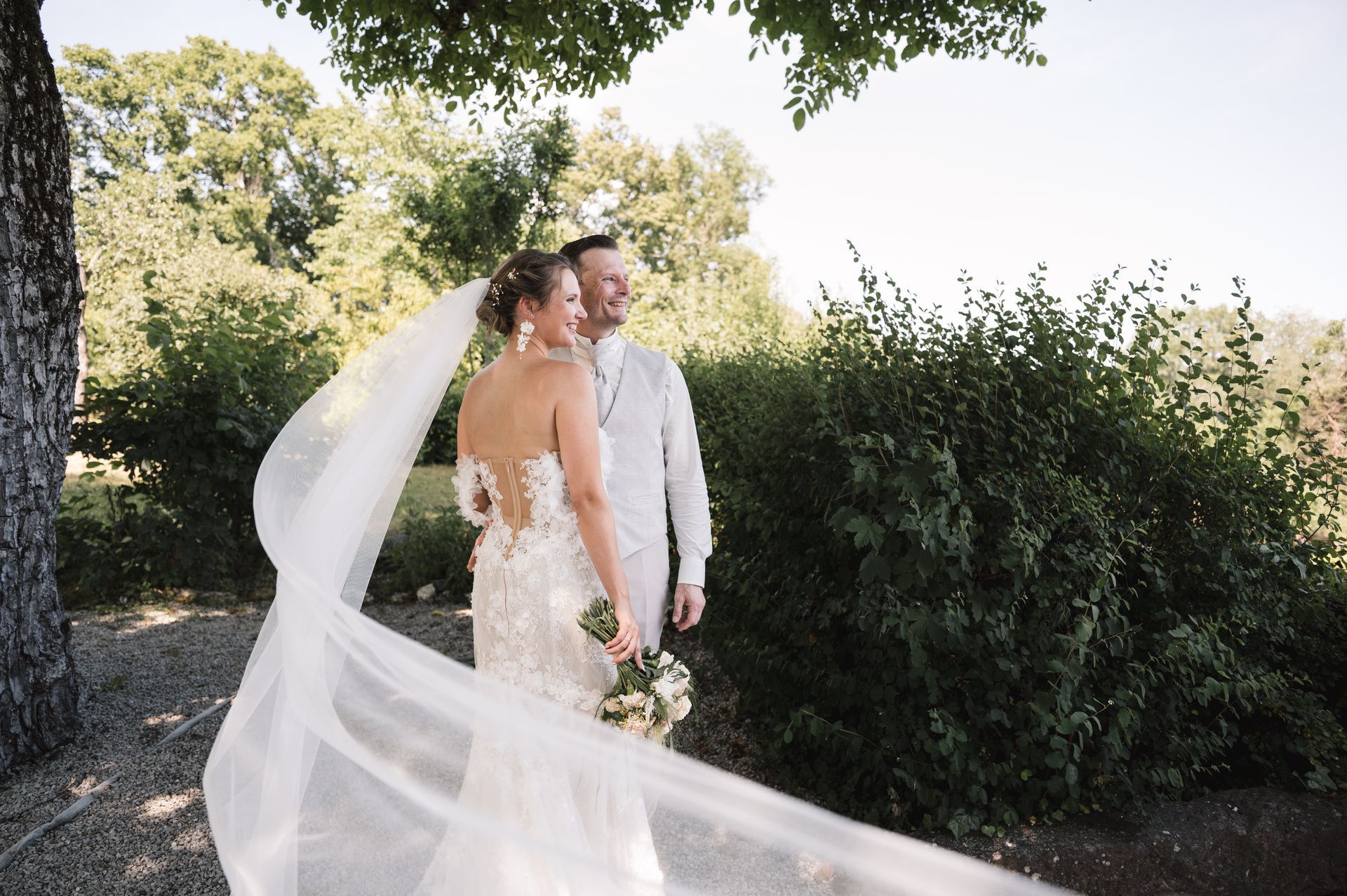 Ein junges Brautpaar steht in der Natur und blickt fröhlich in die Ferne