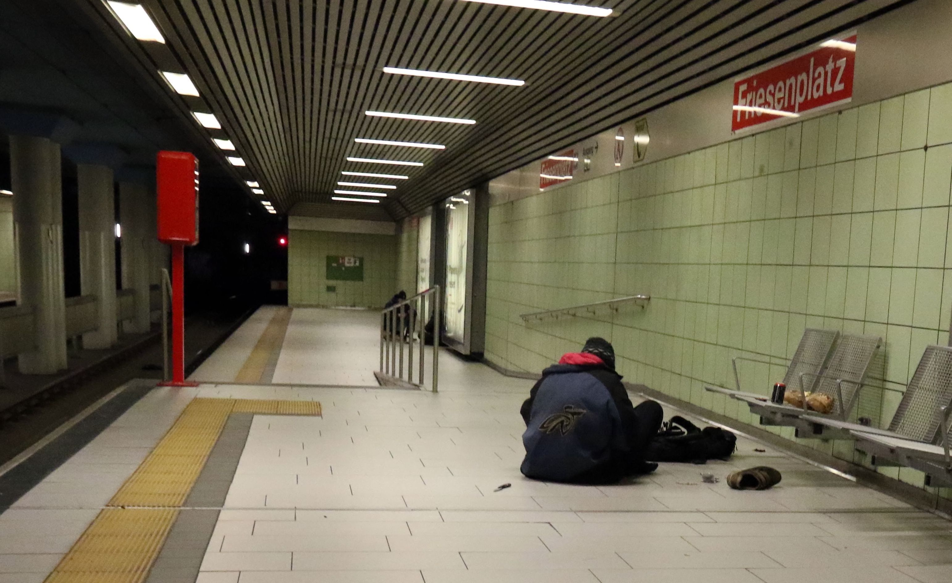 Eine Person sitzt in einer U-Bahnhaltestelle auf dem Boden.