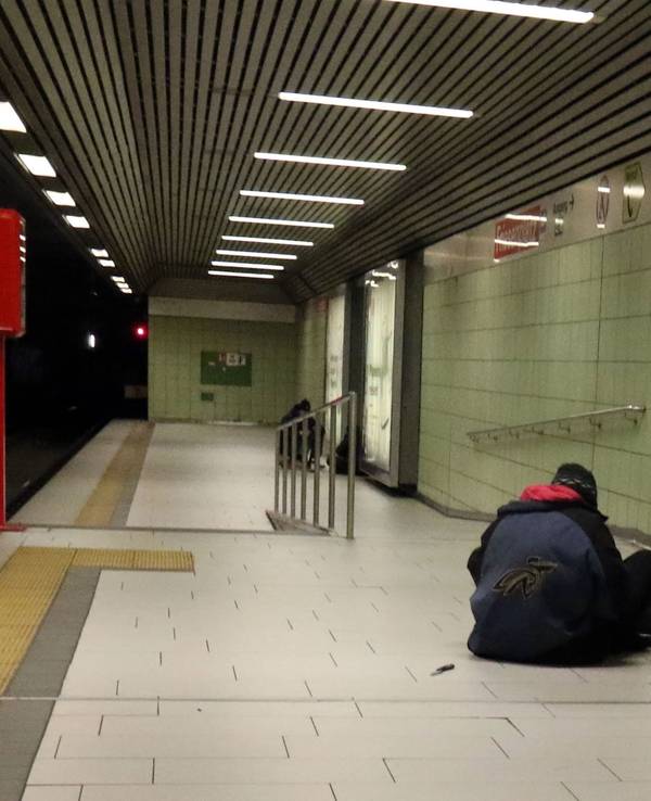 Eine Person sitzt in einer U-Bahnhaltestelle auf dem Boden.