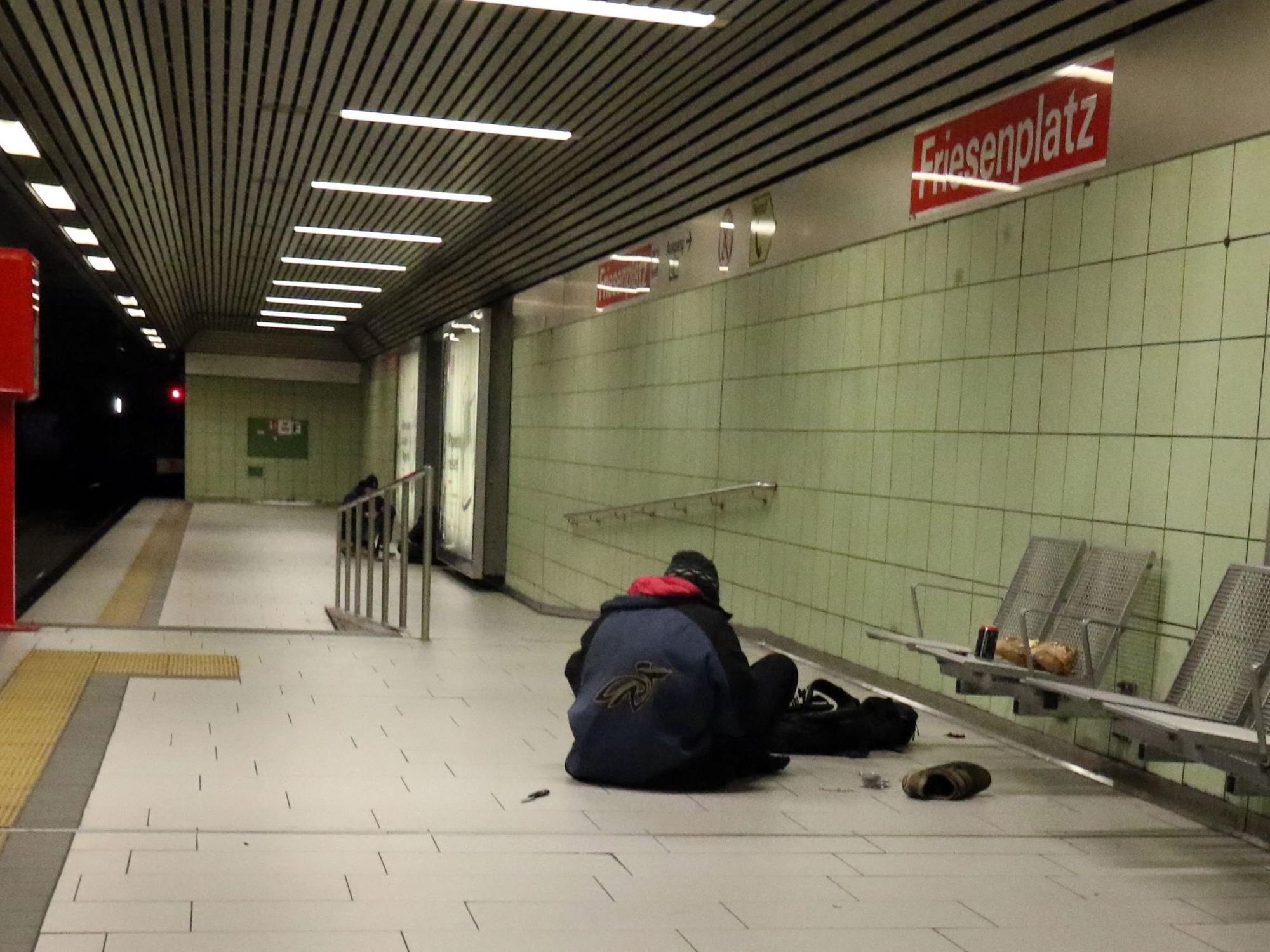Eine Person sitzt in einer U-Bahnhaltestelle auf dem Boden.