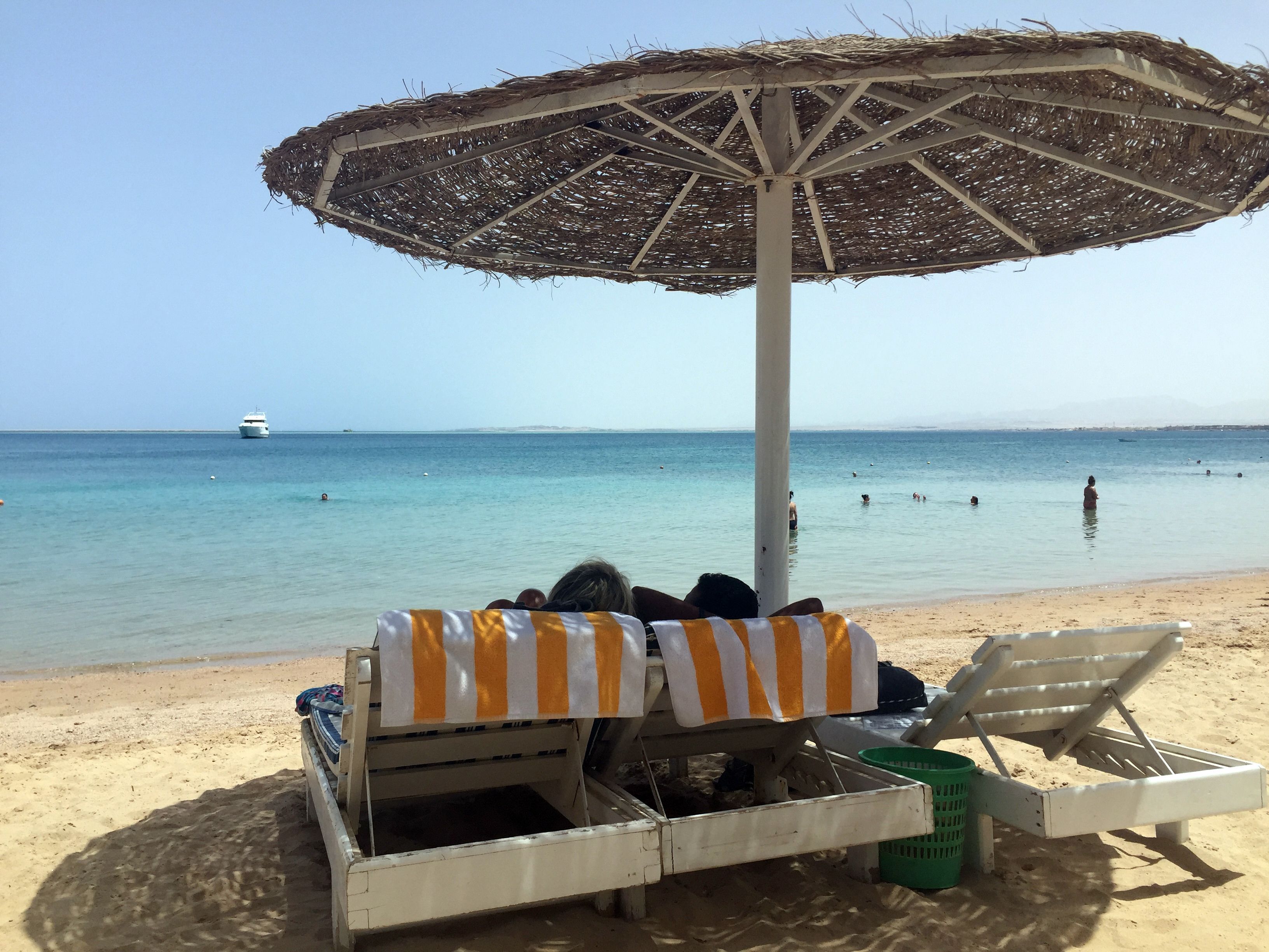 Eine Frau und ein Mann liegen unter einem Sonnenschirm an einem Strand und blicken aufs Meer.