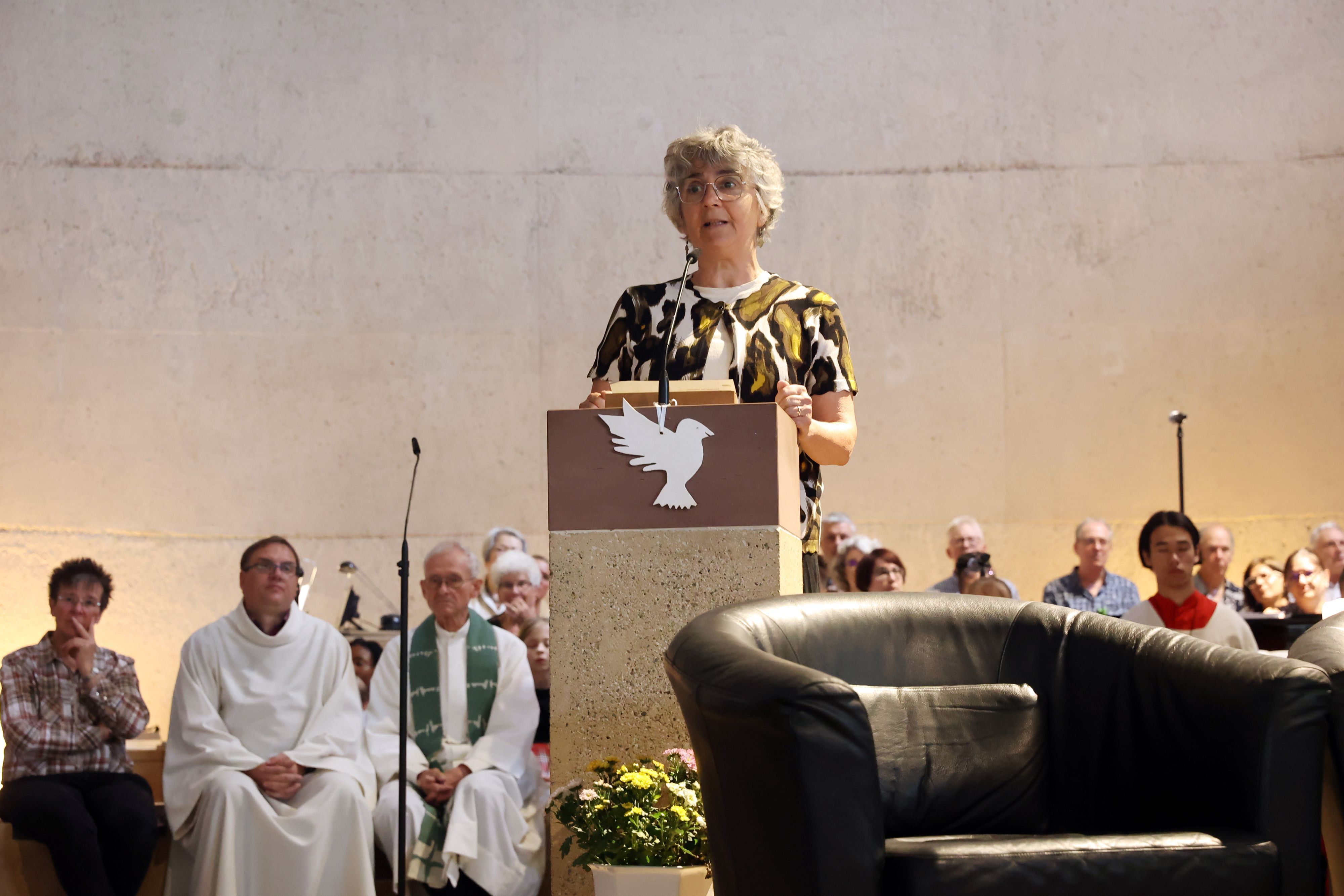 Eine Frau steht am Ambo in einer Kirche. Hinter ihr sind der Chor, der Pfarrer und Messdiener zu sehen.