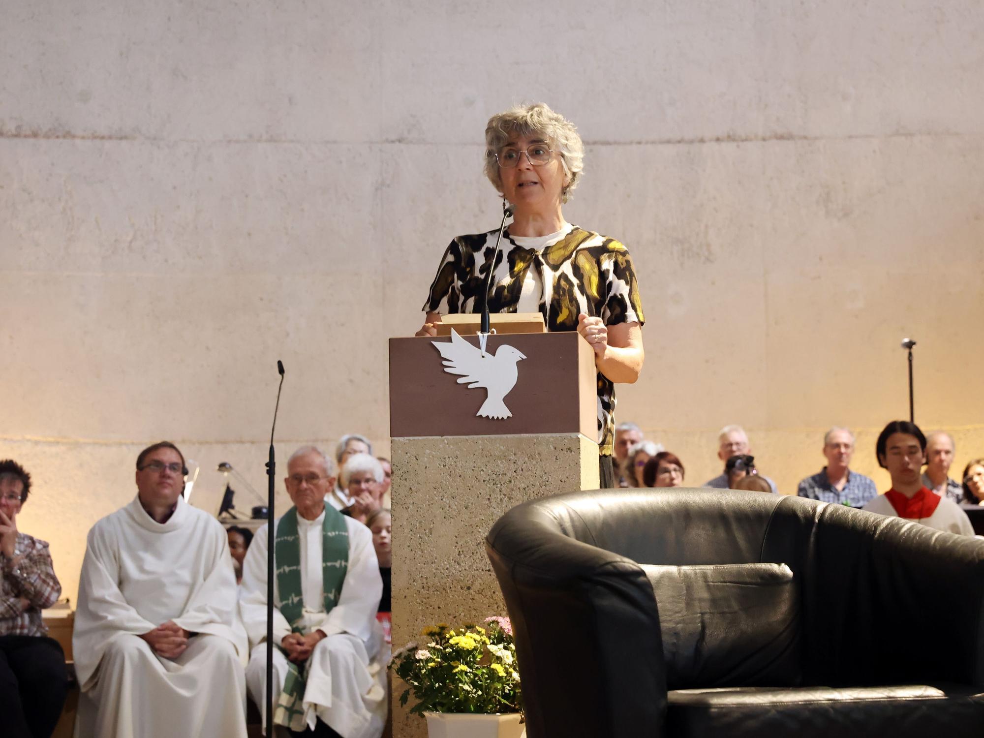 Eine Frau steht am Ambo in einer Kirche. Hinter ihr sind der Chor, der Pfarrer und Messdiener zu sehen.