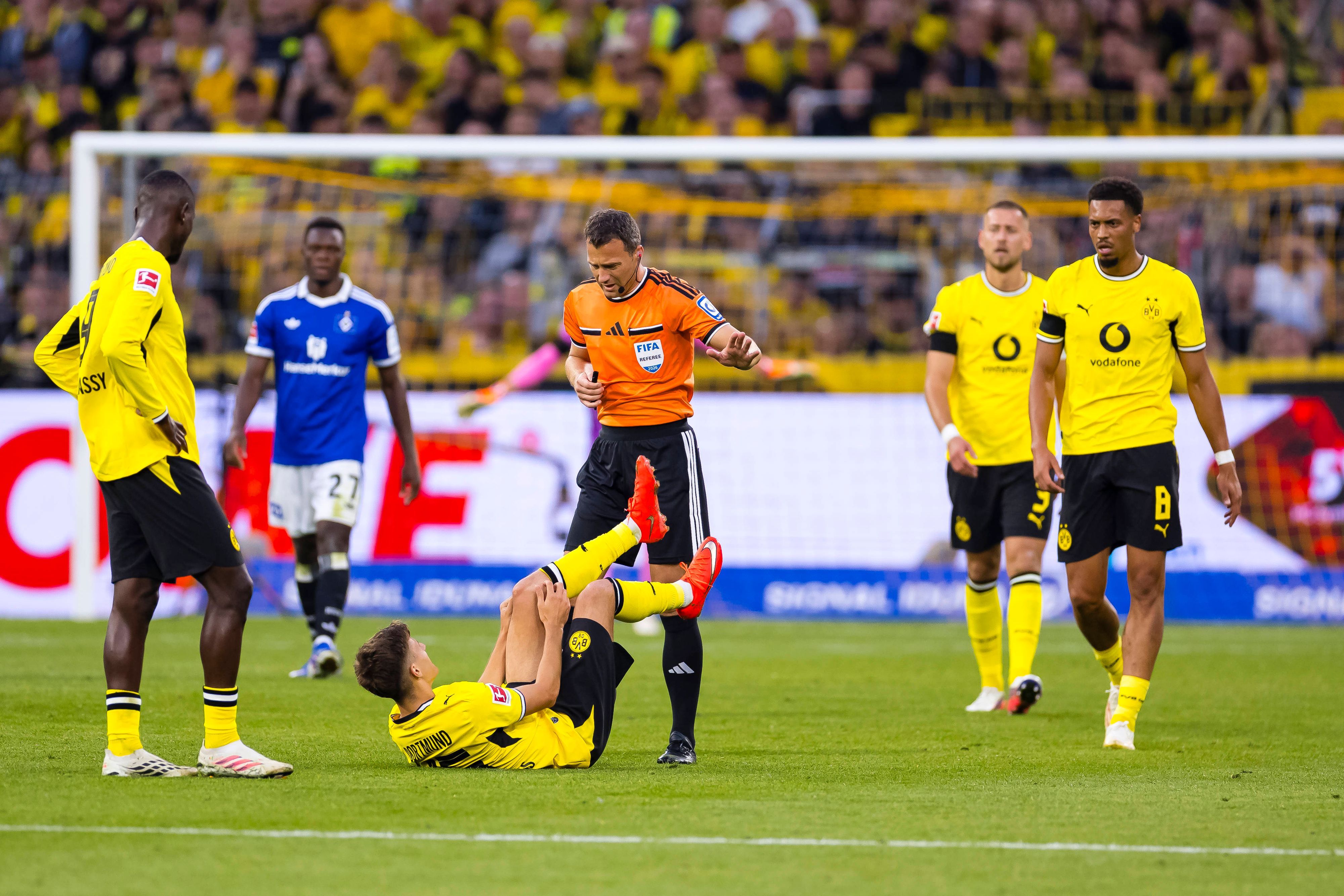 Giannis Konstantelias liegt auf dem Boden und hält sich das Knie. Serhou Guirassy und Felix Zwayer stehen daneben.