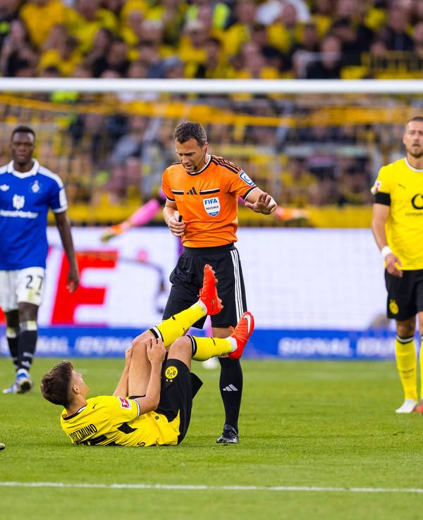 Giannis Konstantelias liegt auf dem Boden und hält sich das Knie. Serhou Guirassy und Felix Zwayer stehen daneben.