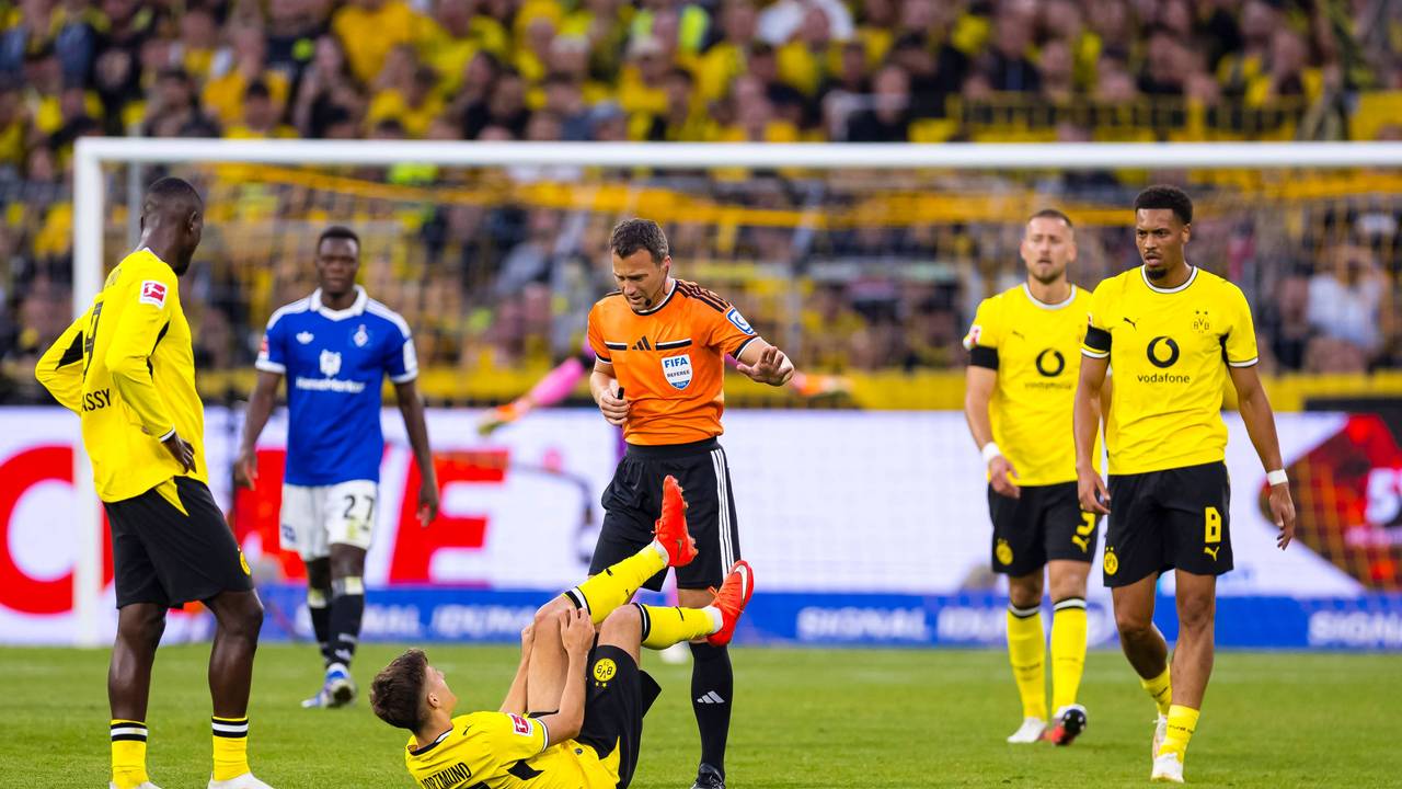 Giannis Konstantelias liegt auf dem Boden und hält sich das Knie. Serhou Guirassy und Felix Zwayer stehen daneben.