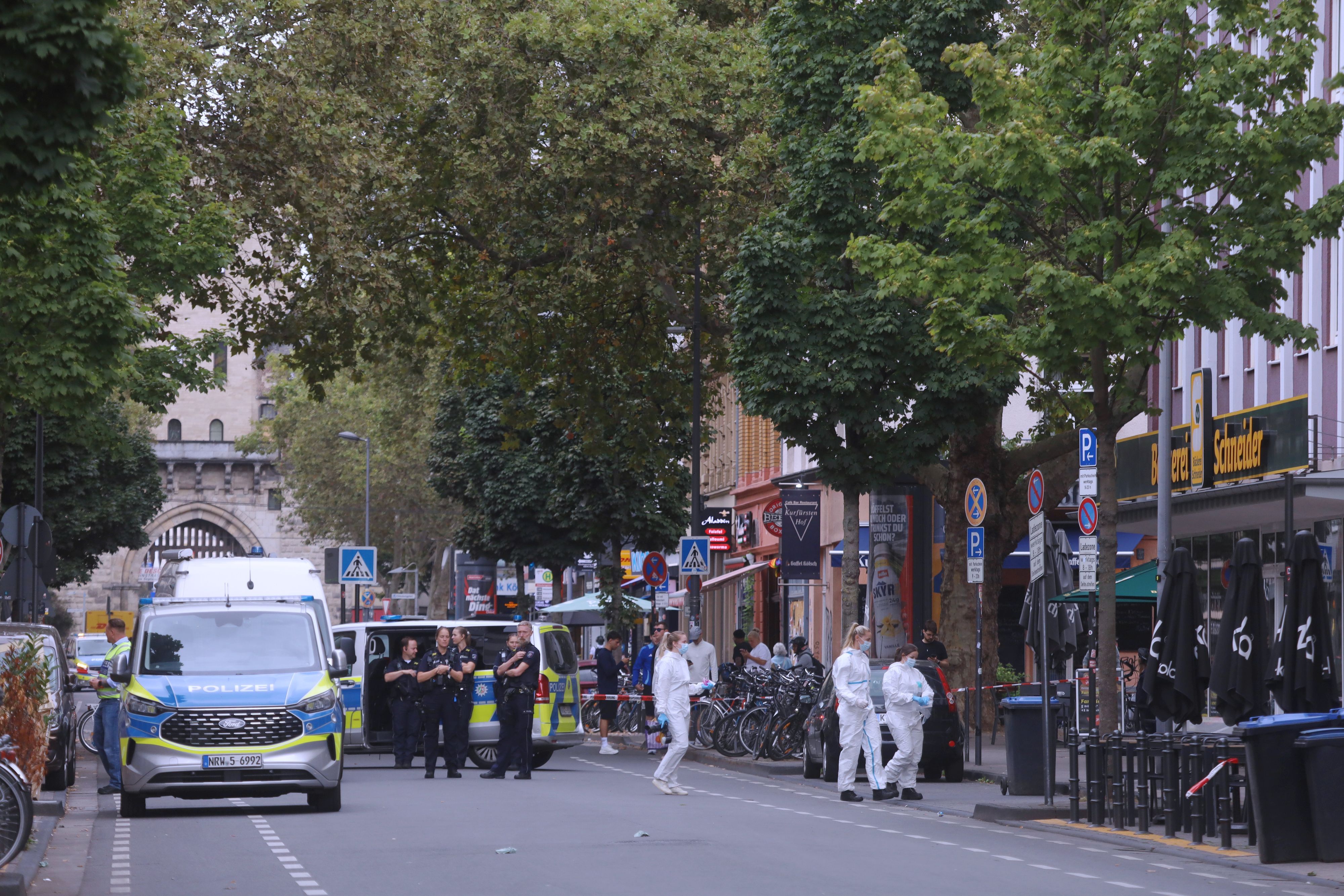 Wagen und Einsatzkräfte der Polizei stehen auf der Bonner Straße, drei Beamtinnen der Spurensicherung sind auf dem Weg zum Tatort.