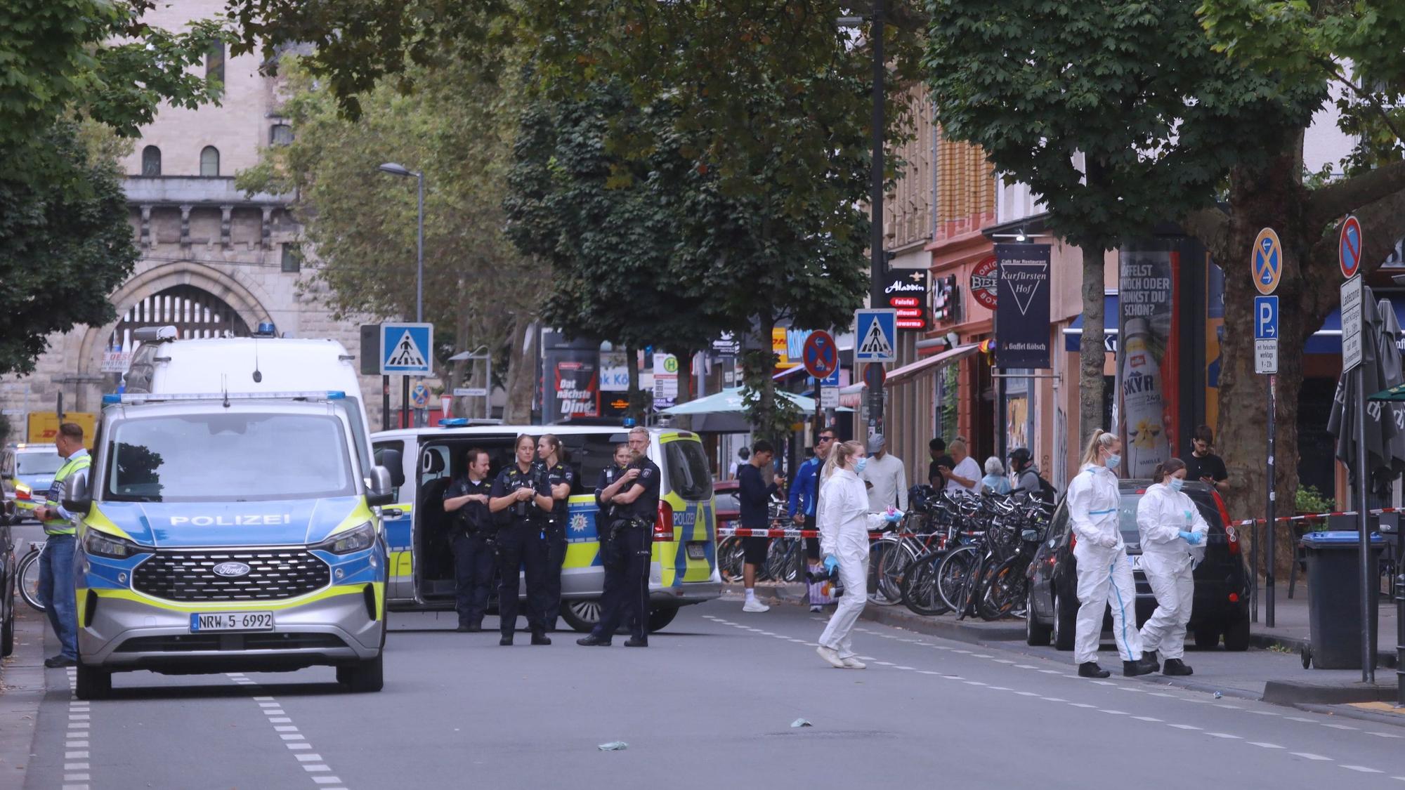 Wagen und Einsatzkräfte der Polizei stehen auf der Bonner Straße, drei Beamtinnen der Spurensicherung sind auf dem Weg zum Tatort.