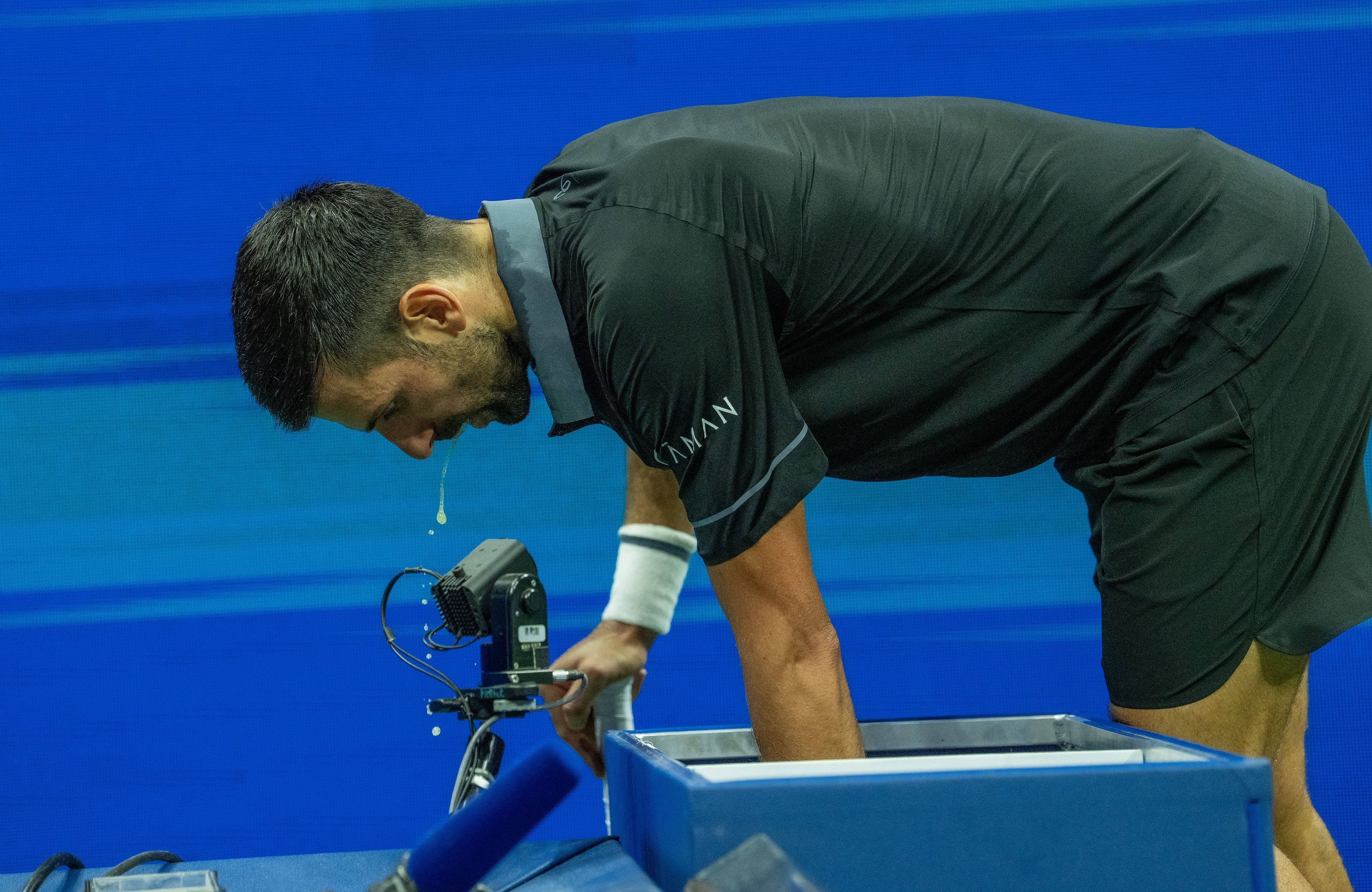 Novak Djokovic beugt sich nach vorne, etwas tropft aus seinem offenen Mund.