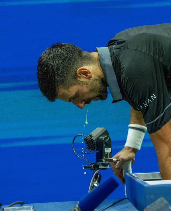 Novak Djokovic beugt sich nach vorne, etwas tropft aus seinem offenen Mund.