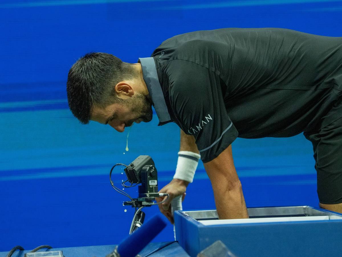 Novak Djokovic beugt sich nach vorne, etwas tropft aus seinem offenen Mund.