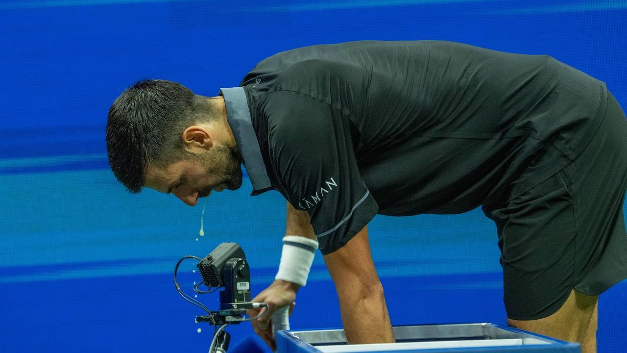 Novak Djokovic beugt sich nach vorne, etwas tropft aus seinem offenen Mund.