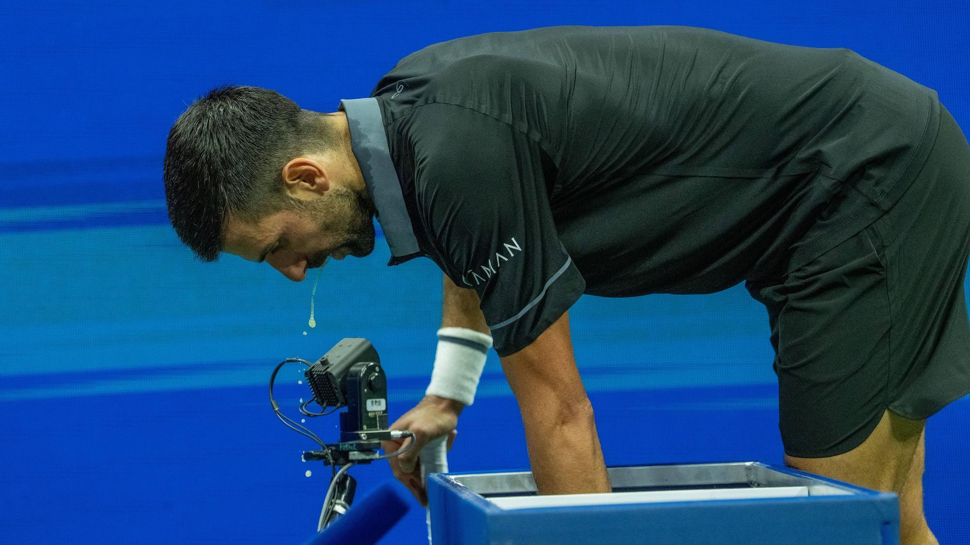 Novak Djokovic beugt sich nach vorne, etwas tropft aus seinem offenen Mund.