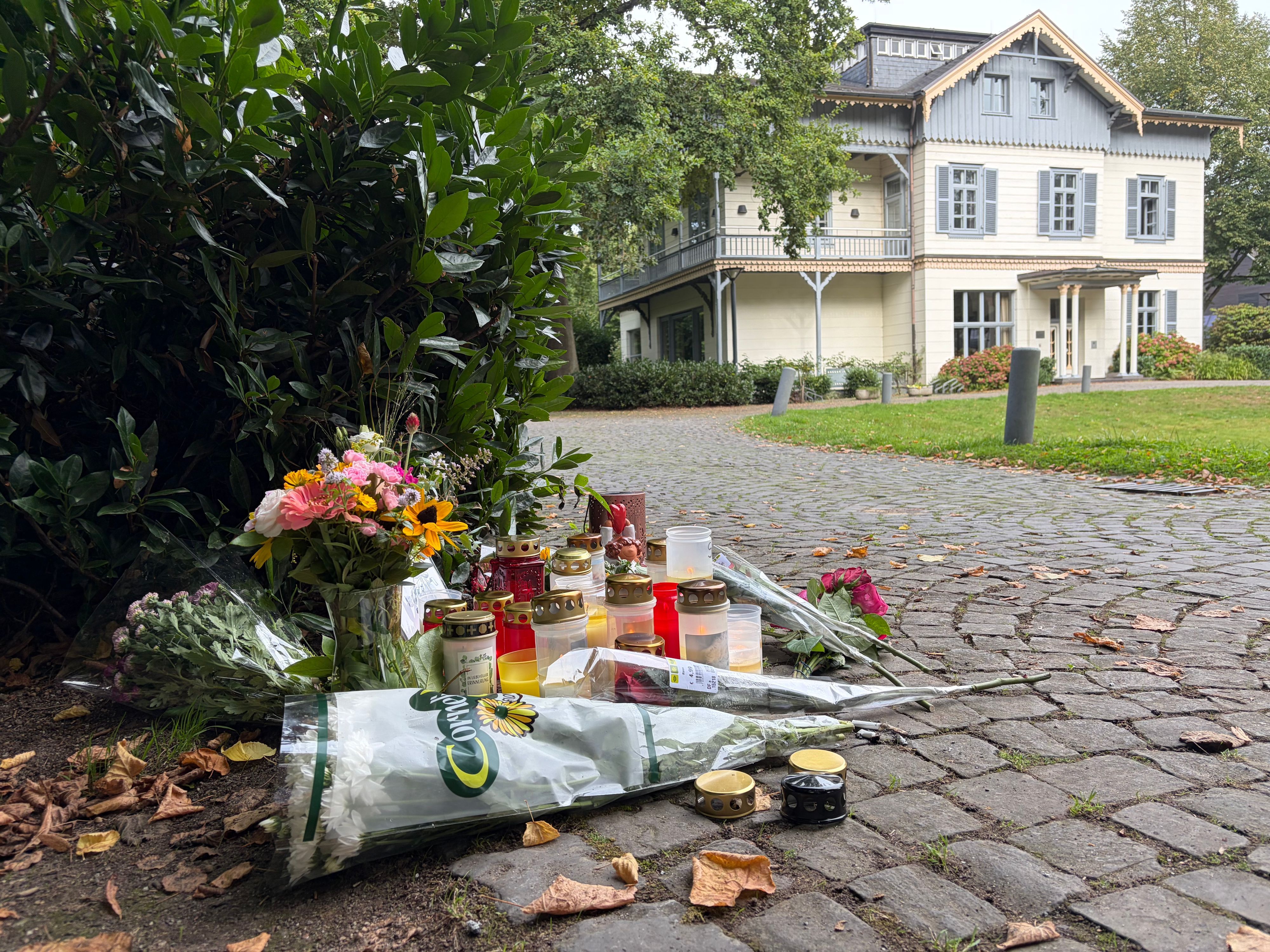 An einem Tatort liegen Blumensträuße, stehen Kerzen.