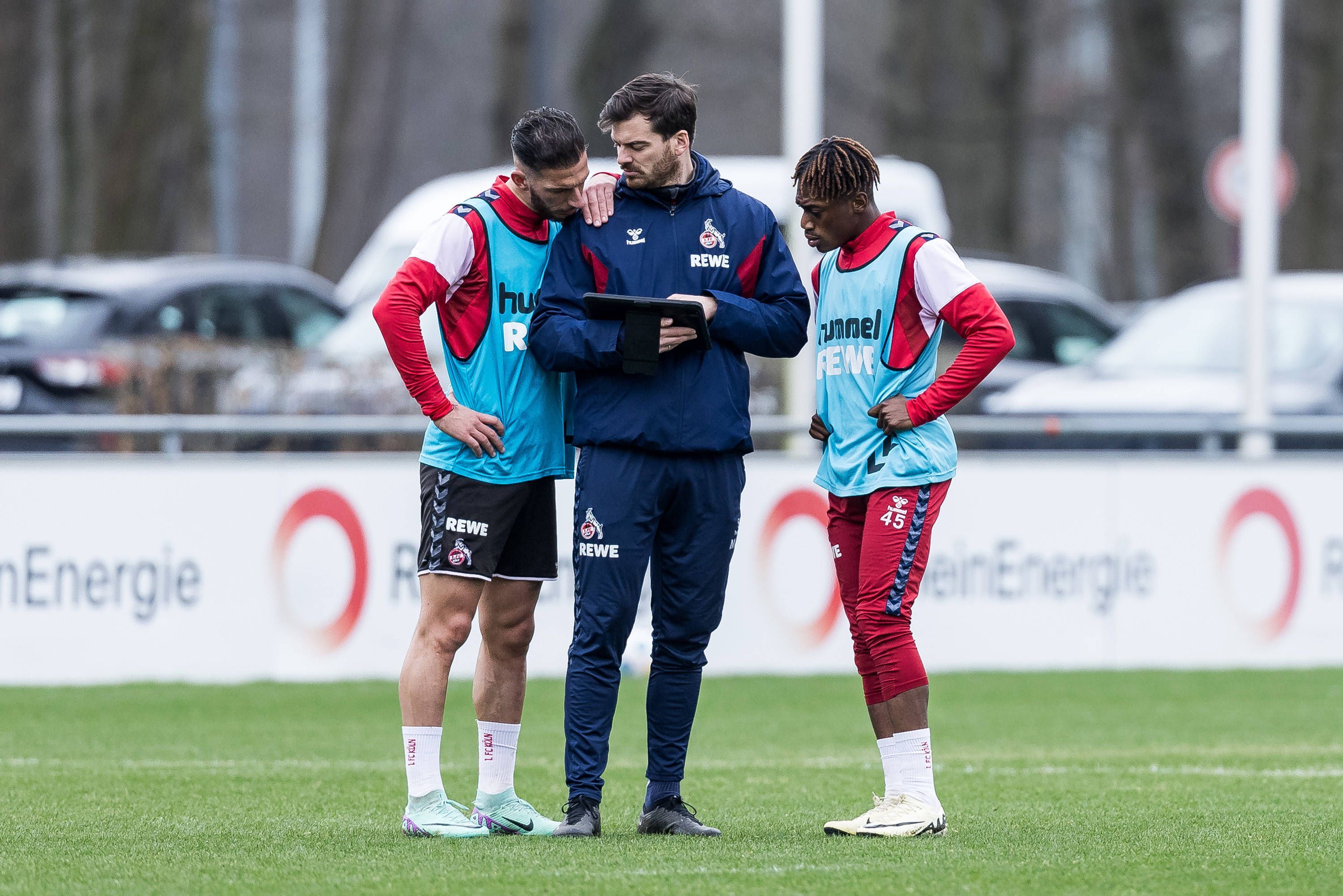 Max Weuthen steht mit Leart Paqarada und Justin Diehl auf dem Trainingsplatz und zeigt ihnen etwas auf dem Tablet.