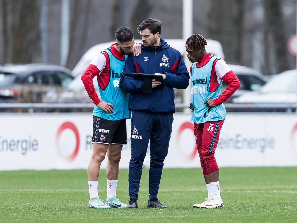 Max Weuthen steht mit Leart Paqarada und Justin Diehl auf dem Trainingsplatz und zeigt ihnen etwas auf dem Tablet.
