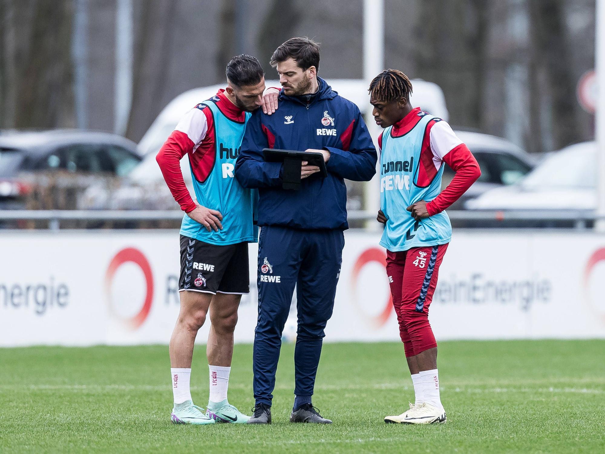 Max Weuthen steht mit Leart Paqarada und Justin Diehl auf dem Trainingsplatz und zeigt ihnen etwas auf dem Tablet.