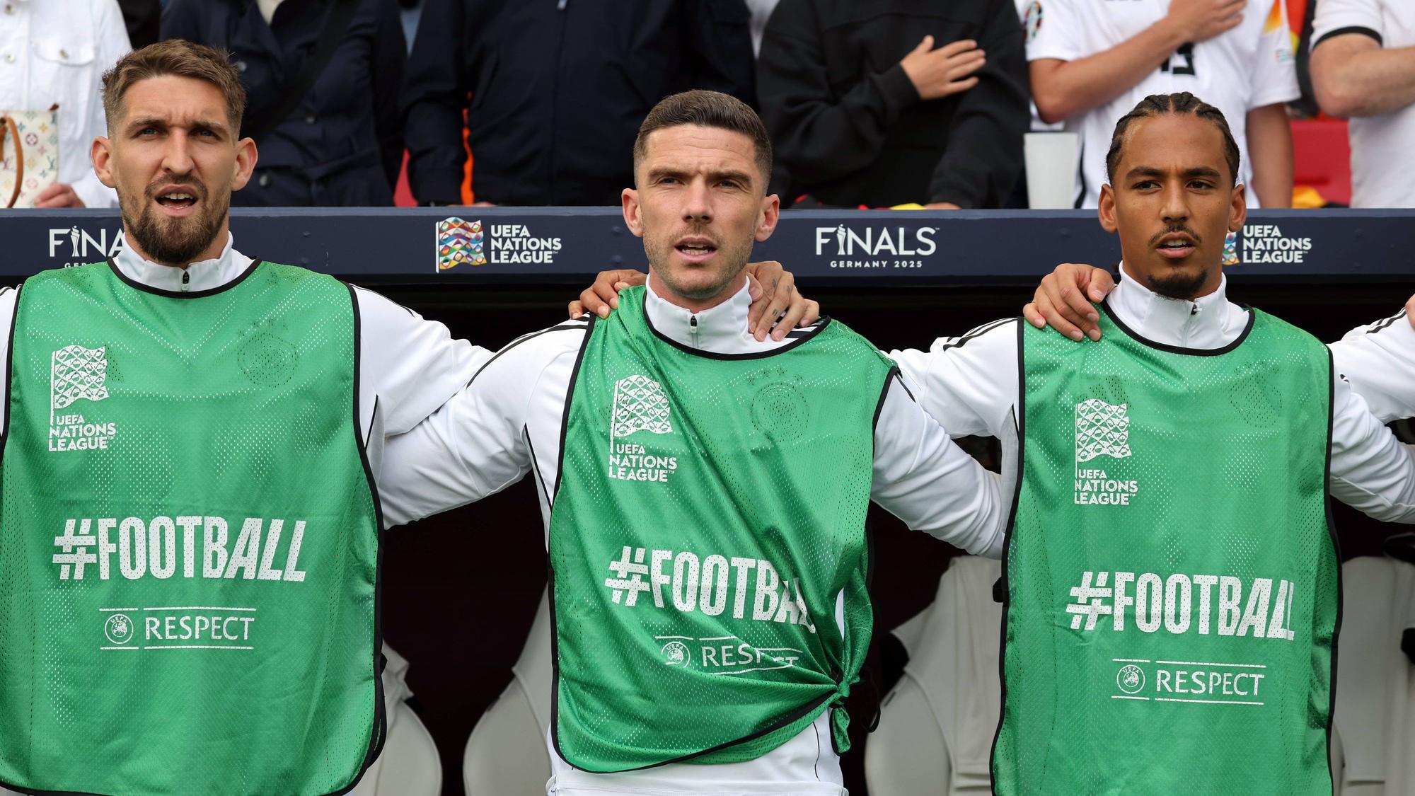 Robert Andrich, Robin Gosens und Thilo Kehrer stehen Arm in Arm und singen die Hymne.