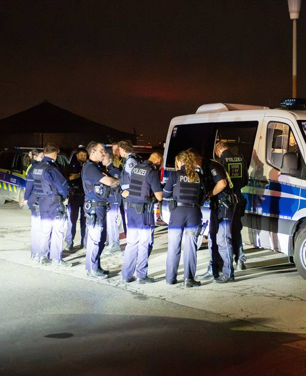 Mehrere Polizeikräfte stehen vor einem Polizeifahrzeug, dahinter stehen weitere Wagen der Polizei.