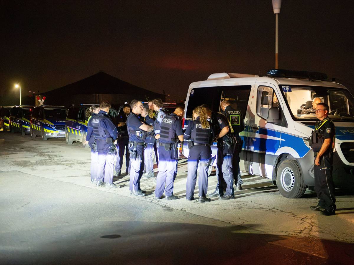 Mehrere Polizeikräfte stehen vor einem Polizeifahrzeug, dahinter stehen weitere Wagen der Polizei.