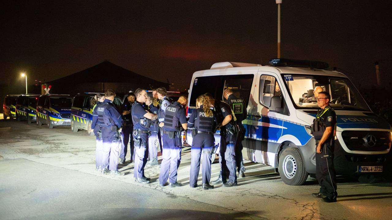 Mehrere Polizeikräfte stehen vor einem Polizeifahrzeug, dahinter stehen weitere Wagen der Polizei.