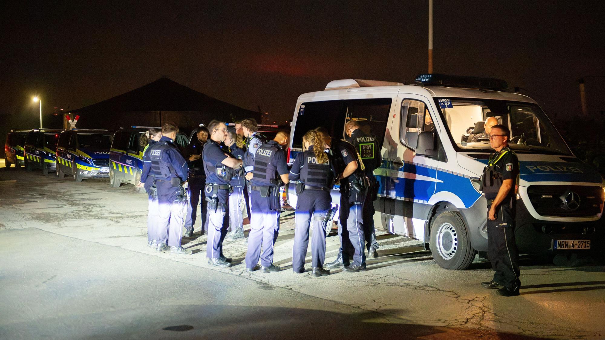 Mehrere Polizeikräfte stehen vor einem Polizeifahrzeug, dahinter stehen weitere Wagen der Polizei.